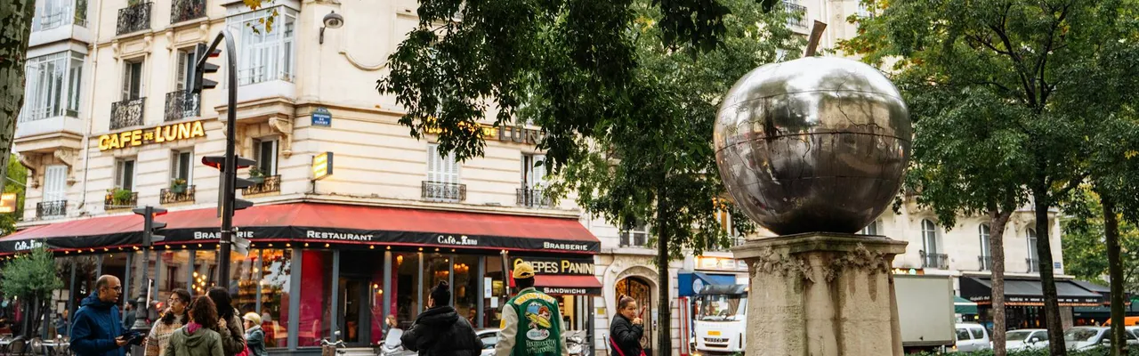A vibrant Paris street scene featuring a cafe, sculpture, and people.