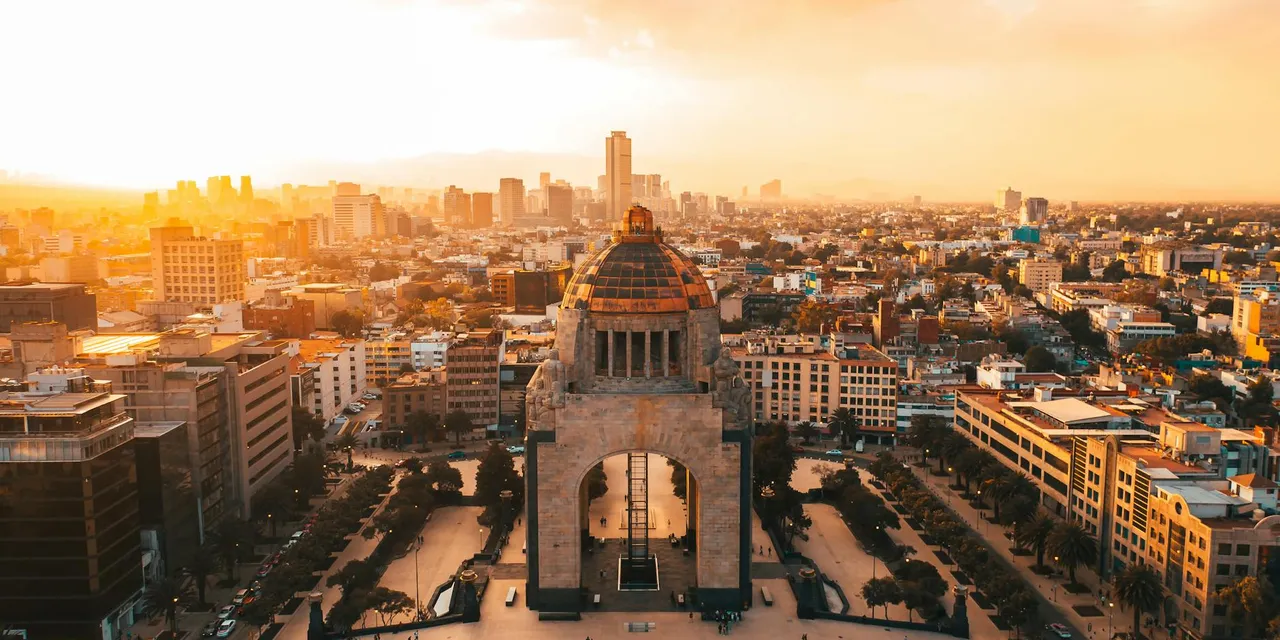 A stunning aerial view of Mexico City's urban landscape at sunset, featuring the iconic Revolution Monument.