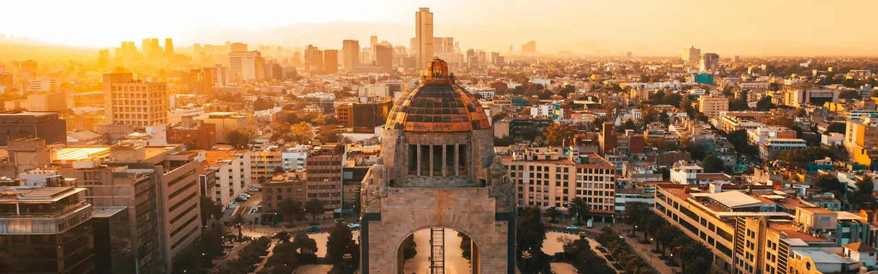 A stunning aerial view of Mexico City's urban landscape at sunset, featuring the iconic Revolution Monument.
