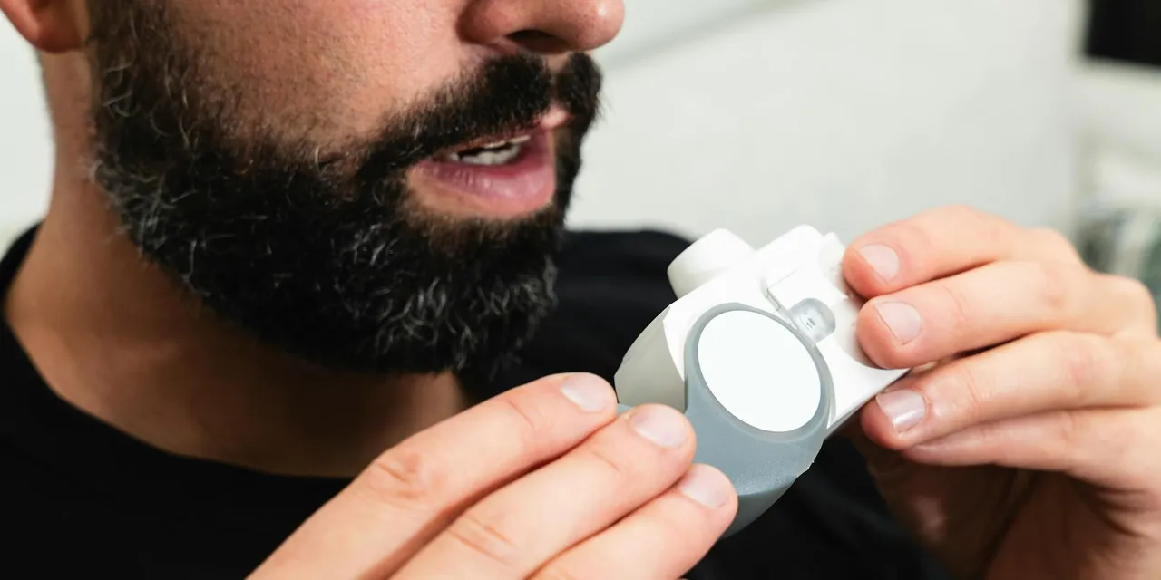 Close-up of a bearded man holding an inhaler, indicating respiratory care.
