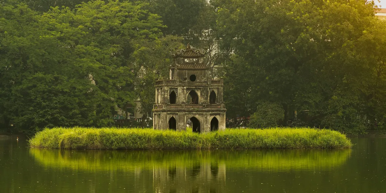 Serene view of Turtle Tower in Hanoi's Hoan Kiem Lake surrounded by lush greenery.