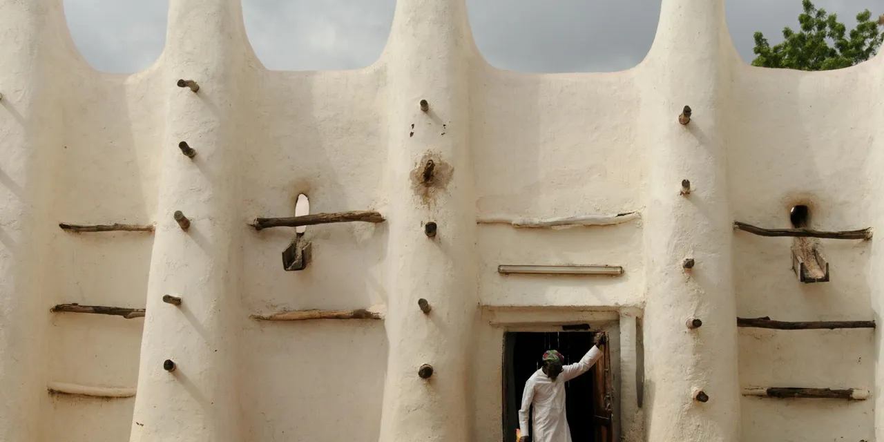 A person entering an adobe mosque with wooden architectural elements in Africa.