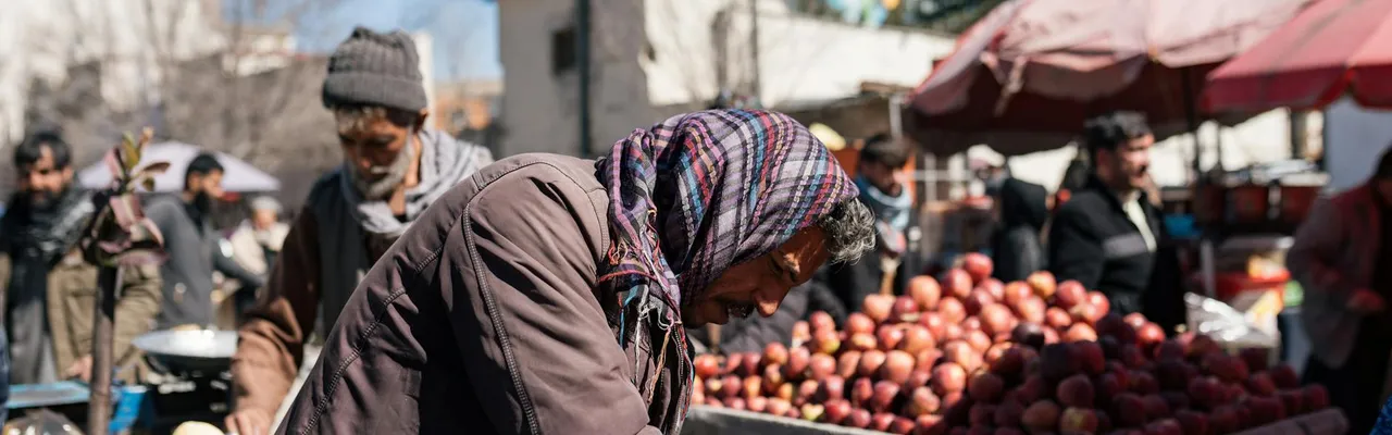 A bustling outdoor market in Afghanistan, showcasing vendors and fresh produce under a clear sky.