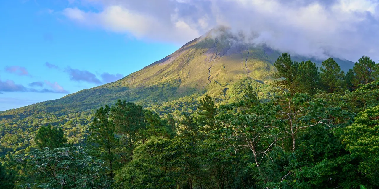 Breathtaking view of a lush green landscape with a majestic volcanic mountain under a cloudy sky.