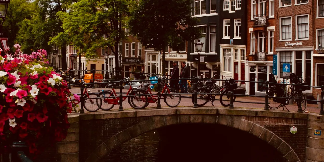 Scenic view of an Amsterdam canal bridge adorned with bicycles and vibrant flowers, perfect for urban travel inspiration.