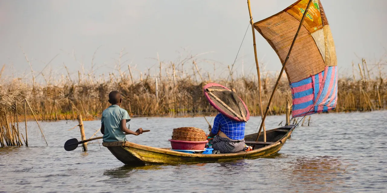 A man and woman paddle a wooden boat on Lake Nokoué near Ganvié, Benin.