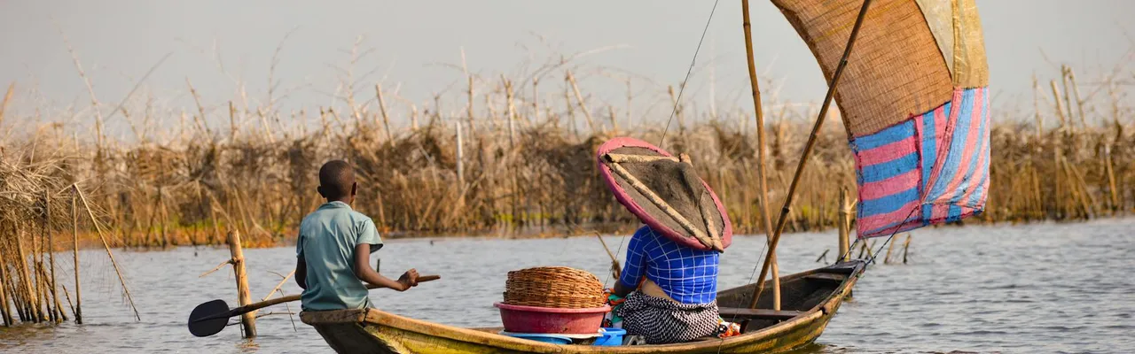 A man and woman paddle a wooden boat on Lake Nokoué near Ganvié, Benin.