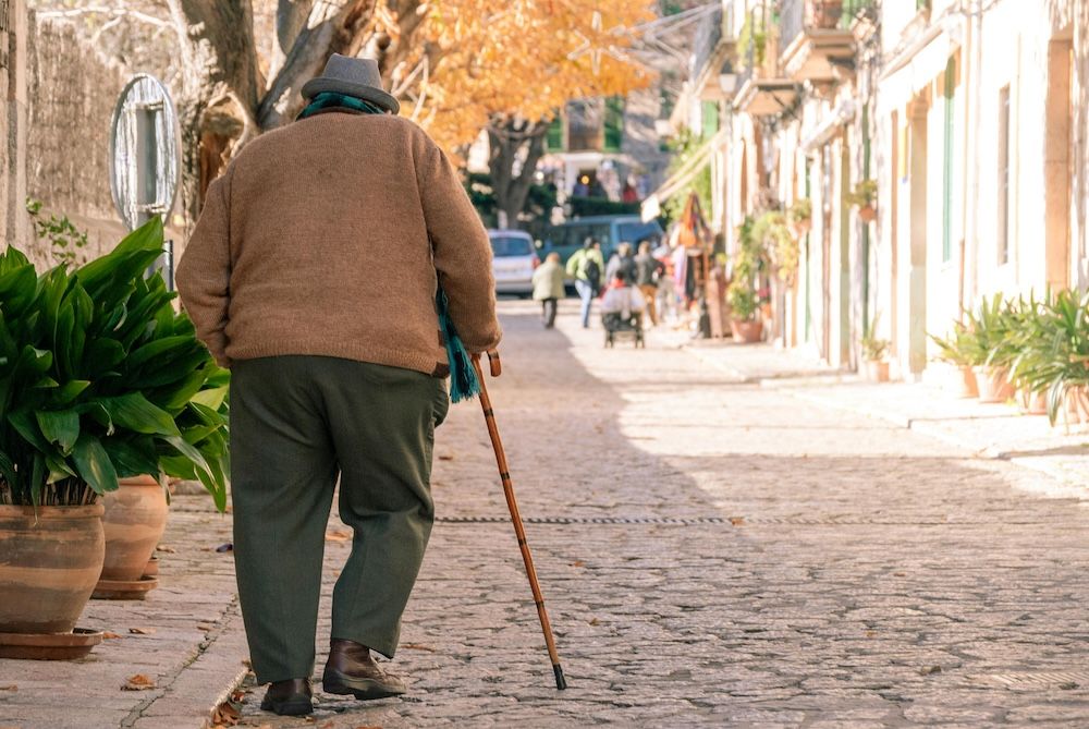 Man travelling in Portugal with Parkinson's disease uses walking stick on cobblestones