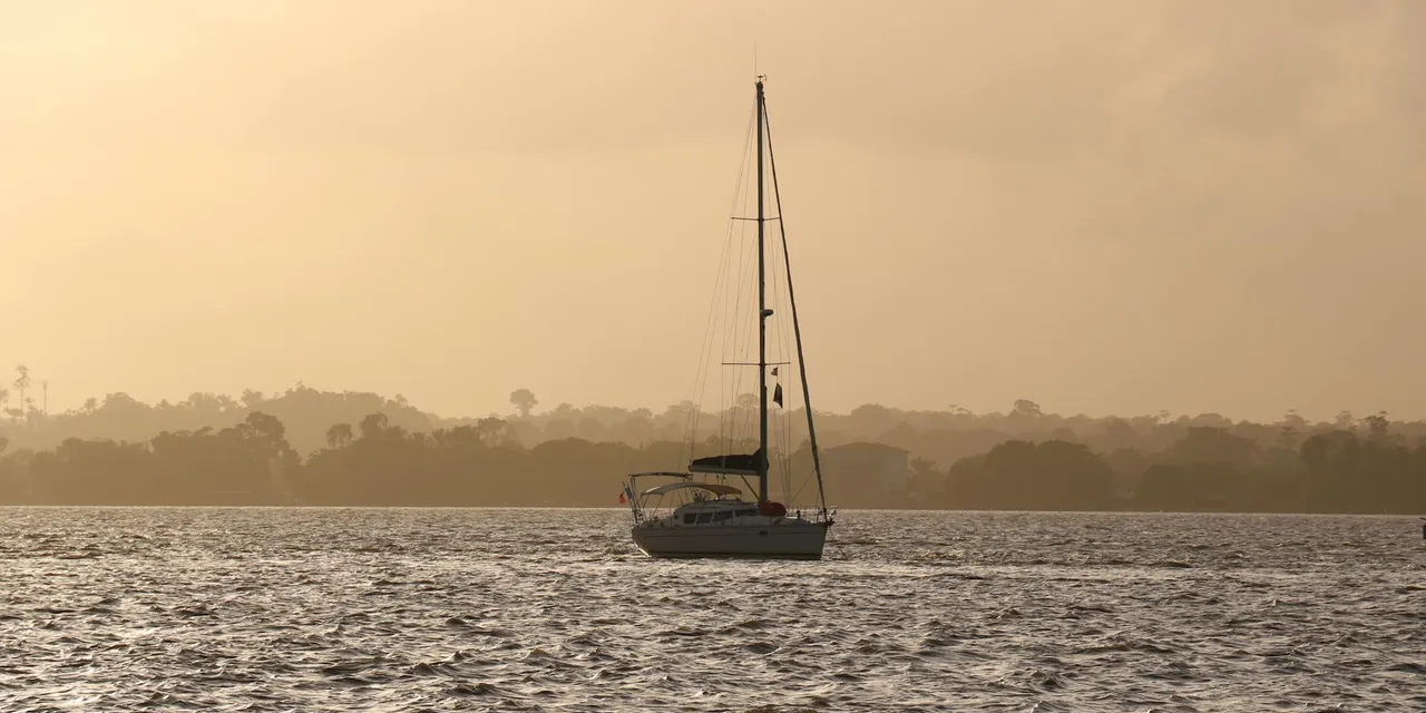 A serene sailboat drifting on the ocean against a warm sunset in French Guiana.