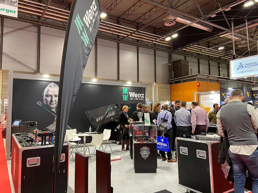 Grupo de visitantes conversando alrededor de las vitrinas de un stand de herramienta en una feria industrial