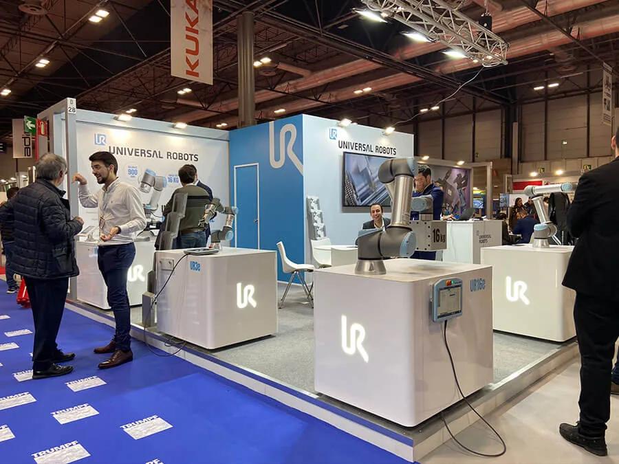 Brazos robóticos colaborativos expuestos y en funcionamiento en un stand de feria industrial, con visitantes atendidos alrededor