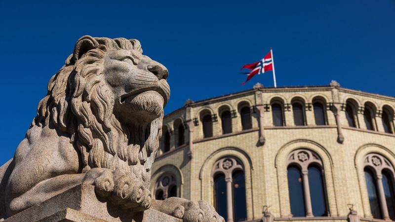 Den ene løven på løvebakken og stortingsbygningen med norsk flagg i bakgrunnen. Foto: Peter Mydske/Stortinget