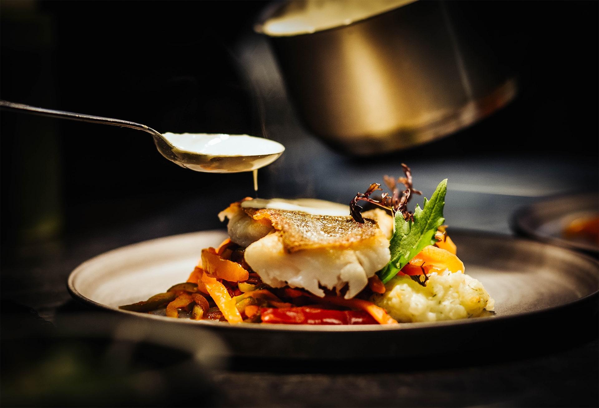 Nærbilde av en middagsrett med fisk som får helt saus på