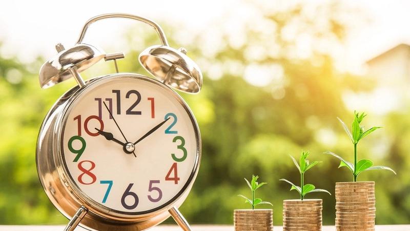 Alarm clock beside stacked coins with growing plants.