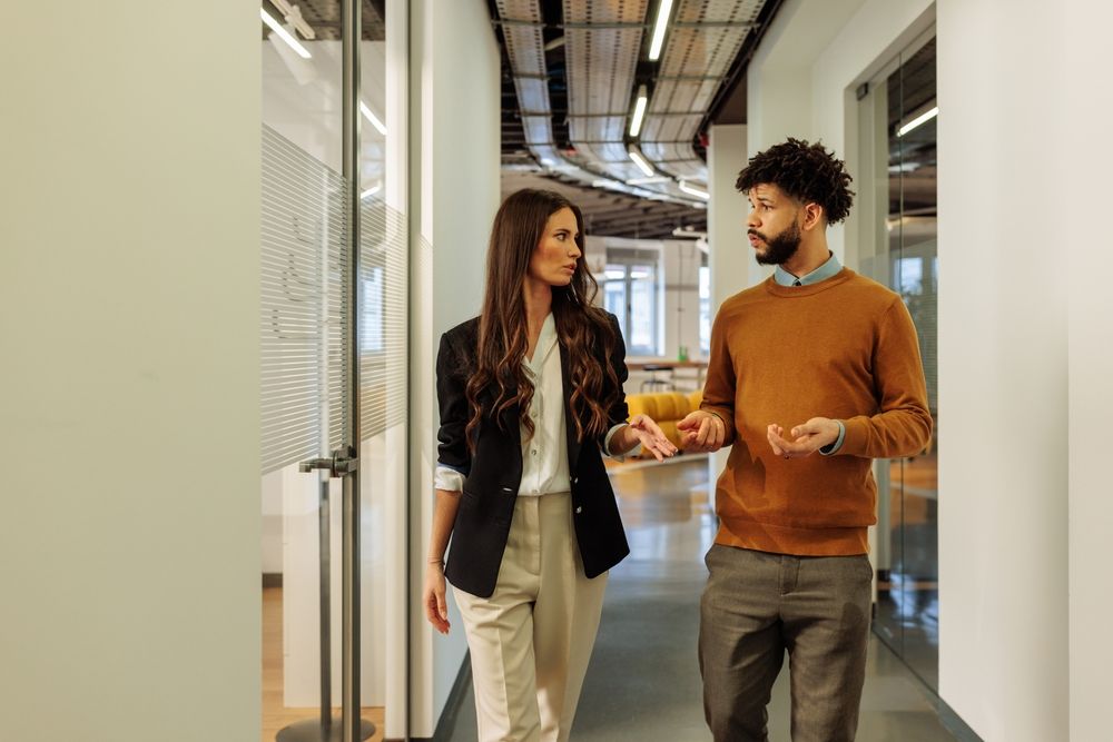 Two employees discussing pay concerns in office hallway related to wage discrimination and unequal pay in the workplace