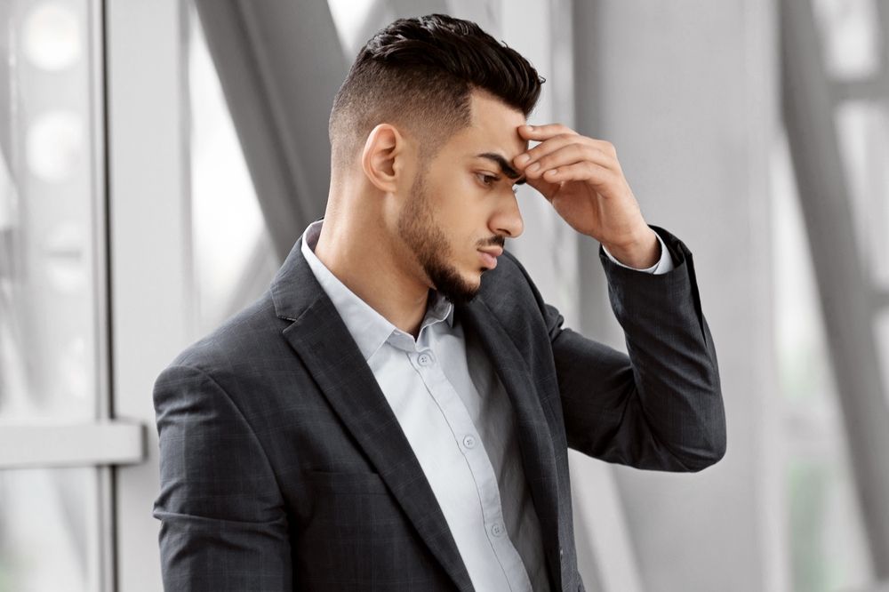 Stressed man in a suit holding his head after a wrongful termination in New Jersey, representing the emotional impact of year-end job loss.