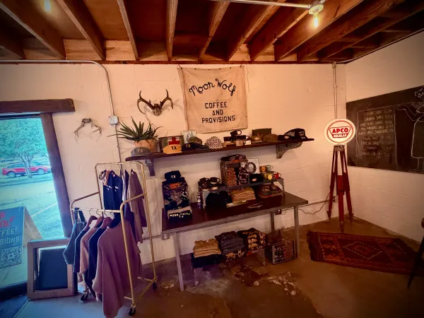 The Moon Wolf Provisions interior at 920 Custer Rd, Richardson TX — Moon Wolf banner over the merch shelf, exposed beams, antler mount, and APCO sign on opening day
