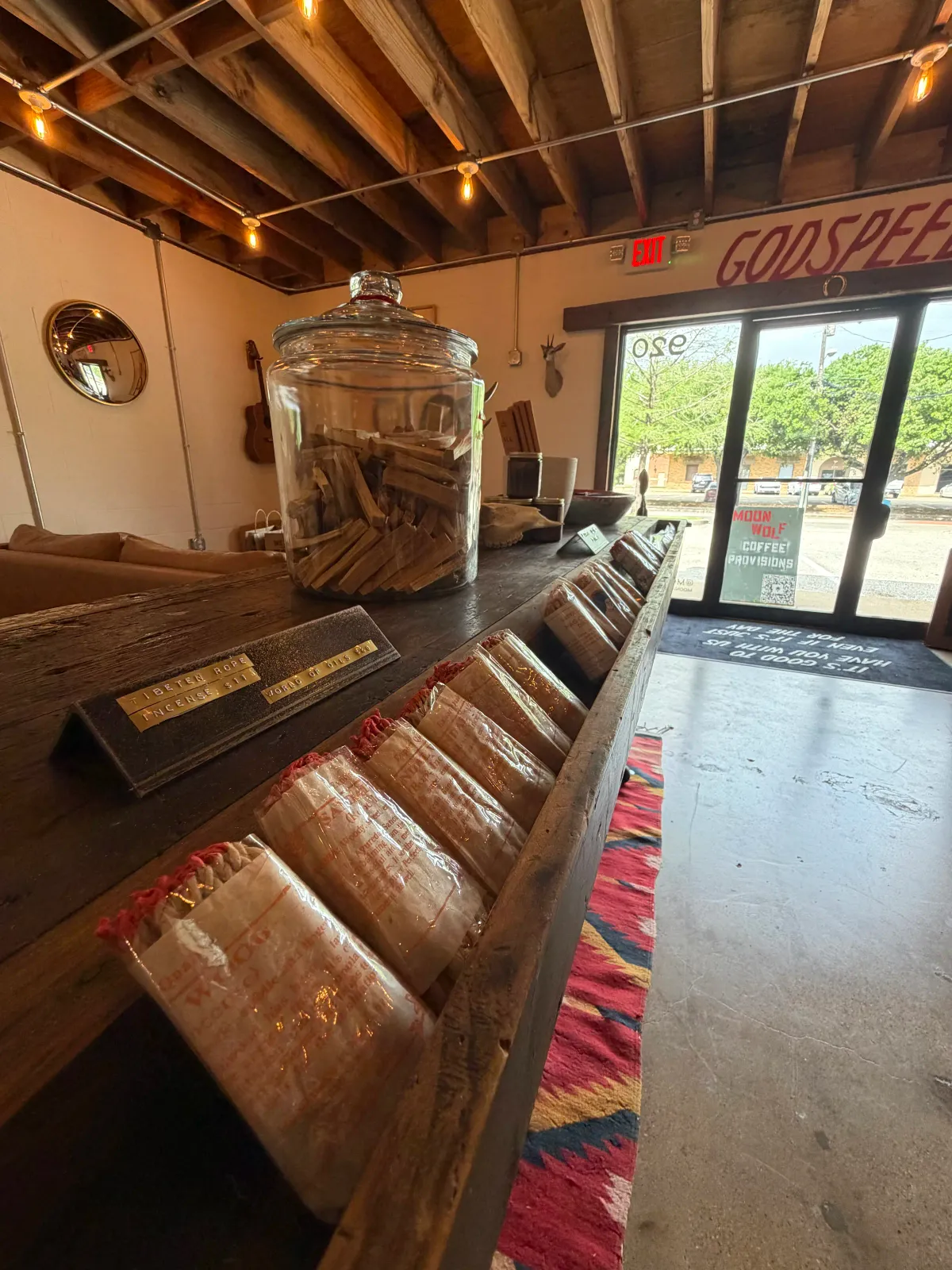 Reclaimed wood retail shelves with paper-wrapped handmade goods and a large glass apothecary jar at Moon Wolf Provisions coffee shop and general store in Richardson Texas