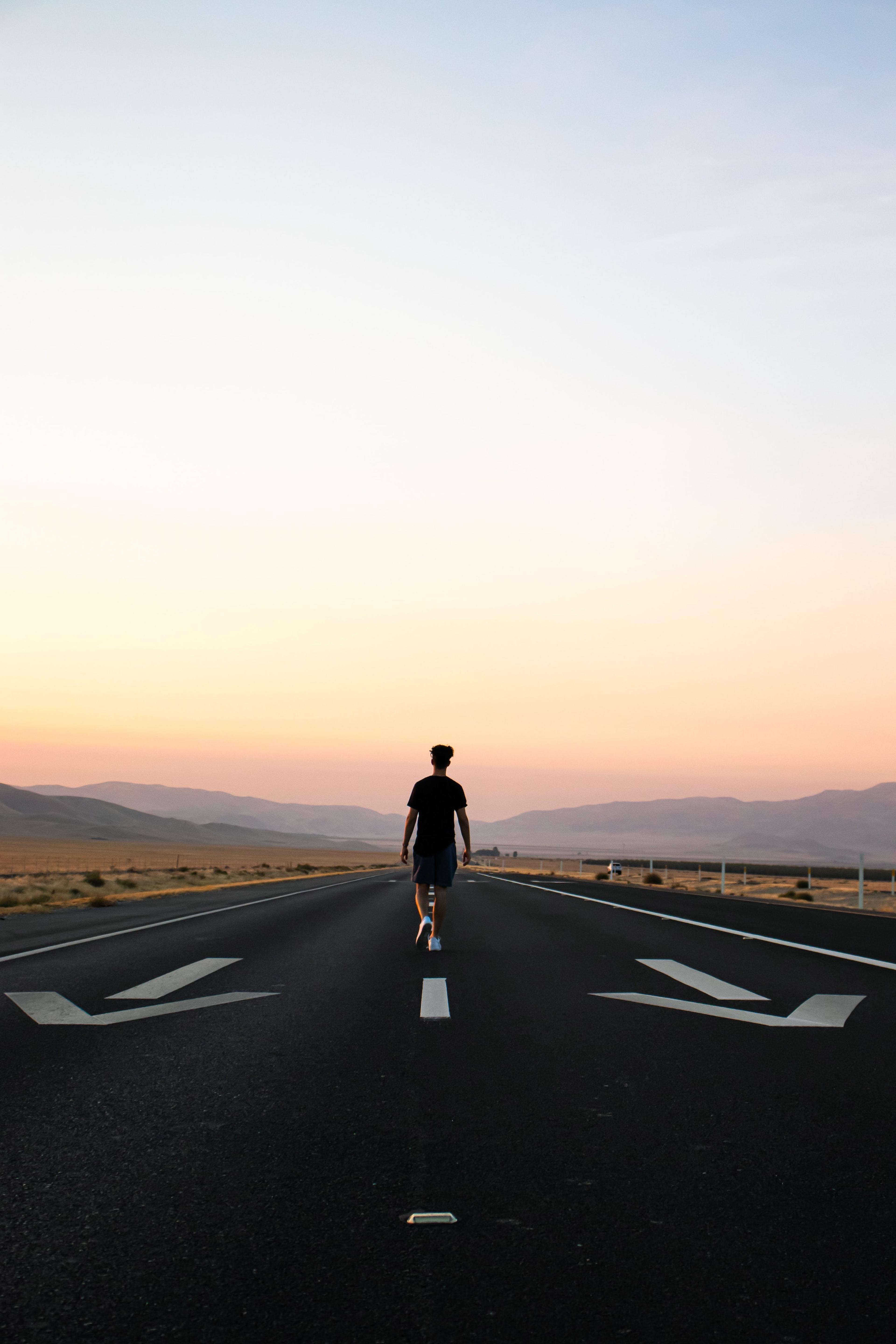 Man walking down airplane runway towards sunset in distance