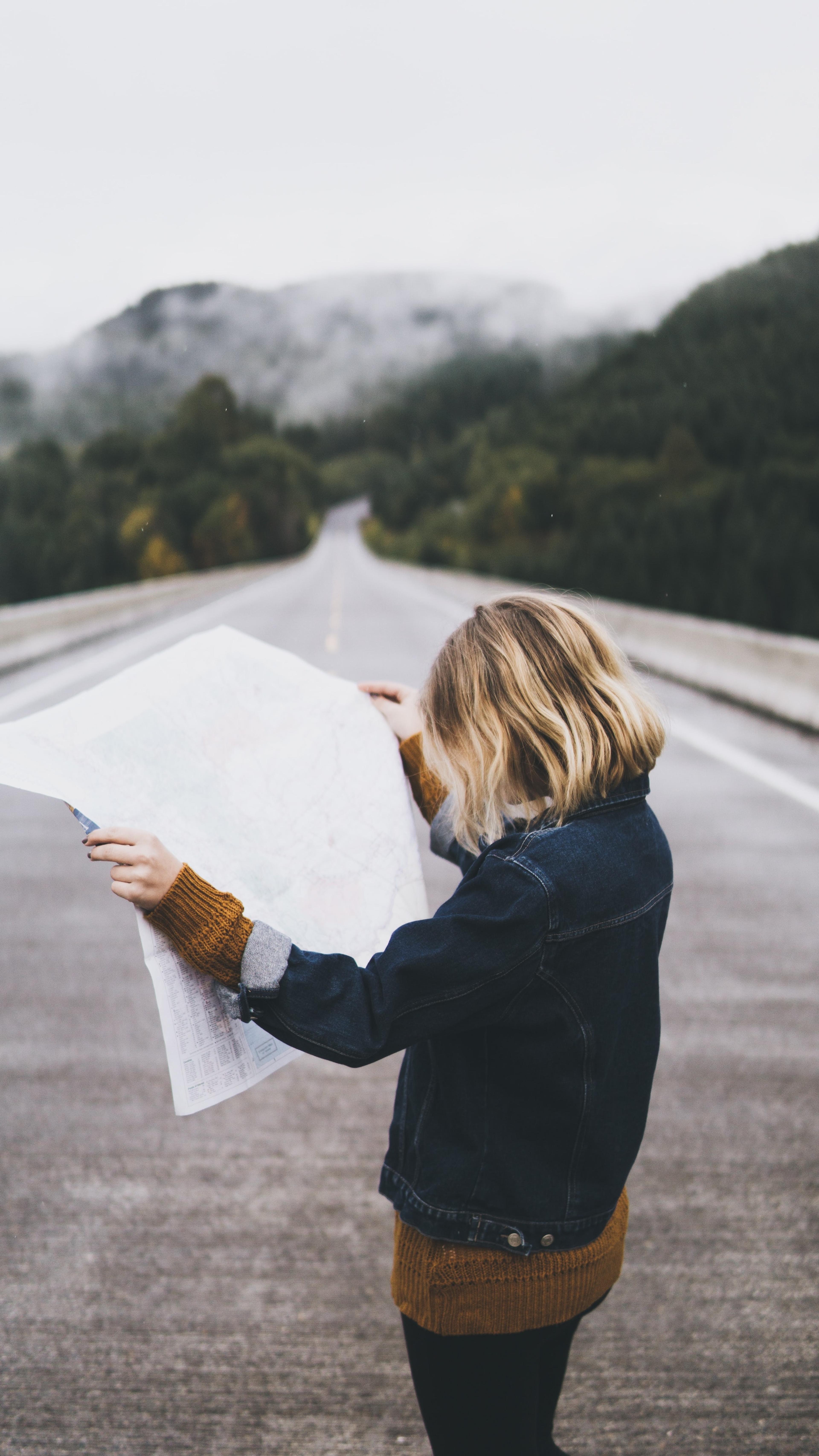 Woman looking at map standing in middle of mountainous road