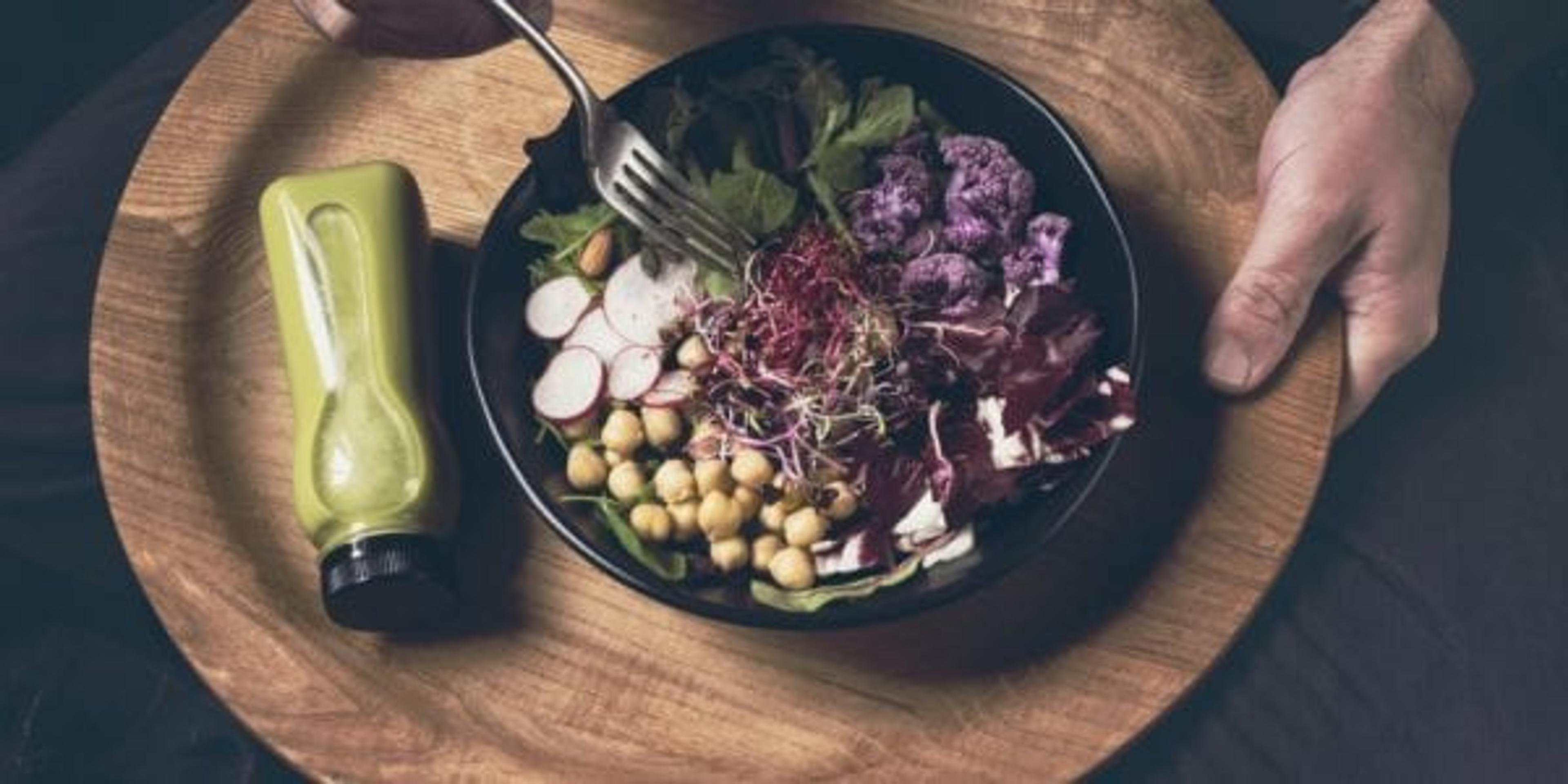 Healthy dinner, lunch in the sofa. Man eating vegan superbowl or Buddha bowl with vegetables, fresh salad, chickpeas, soybean sprouts, purple broccoli