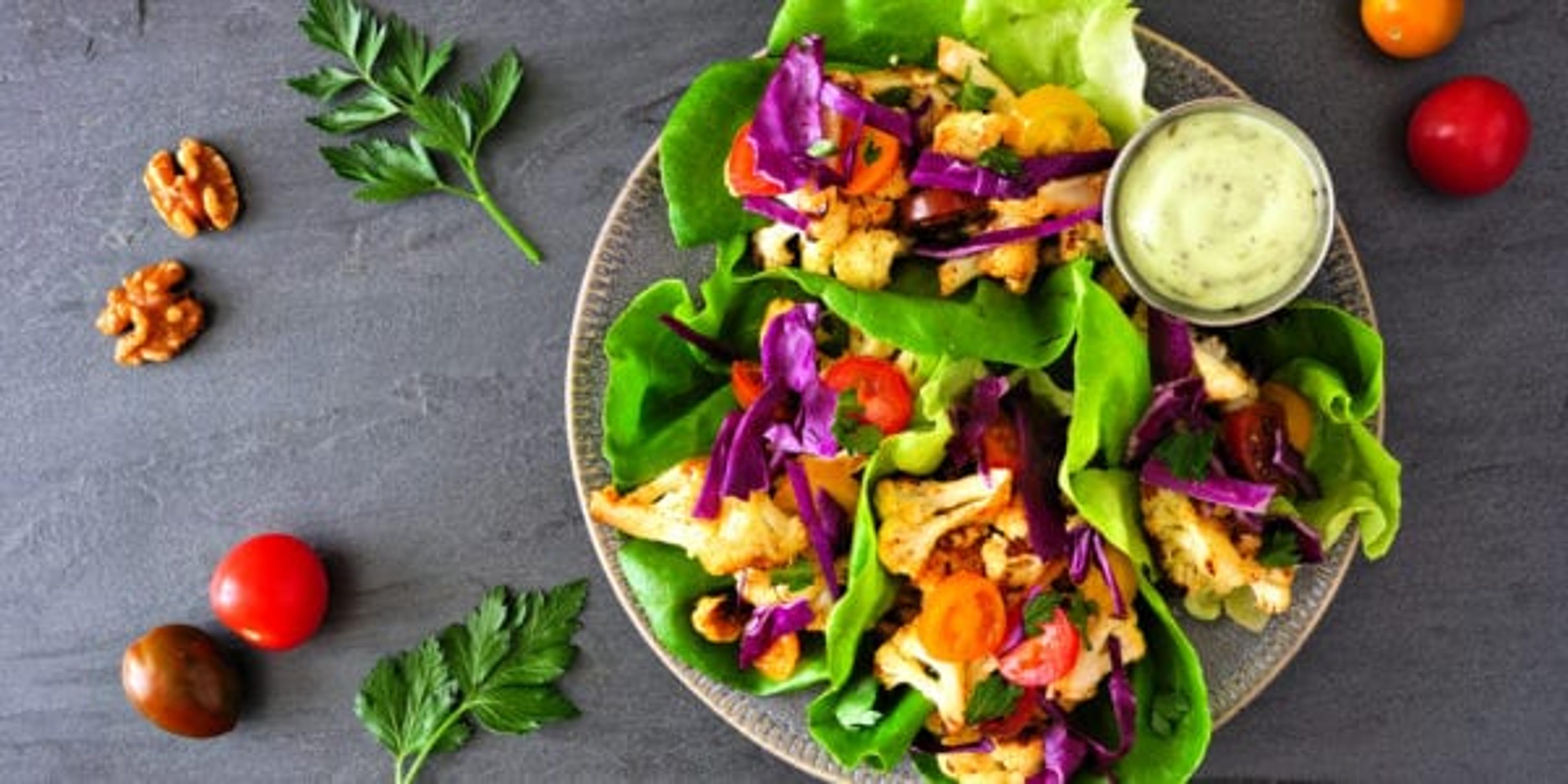 Healthy lettuce wraps with grilled cauliflower, cabbage and tomatoes. Top view over a dark slate background. Plant-based diet concept.