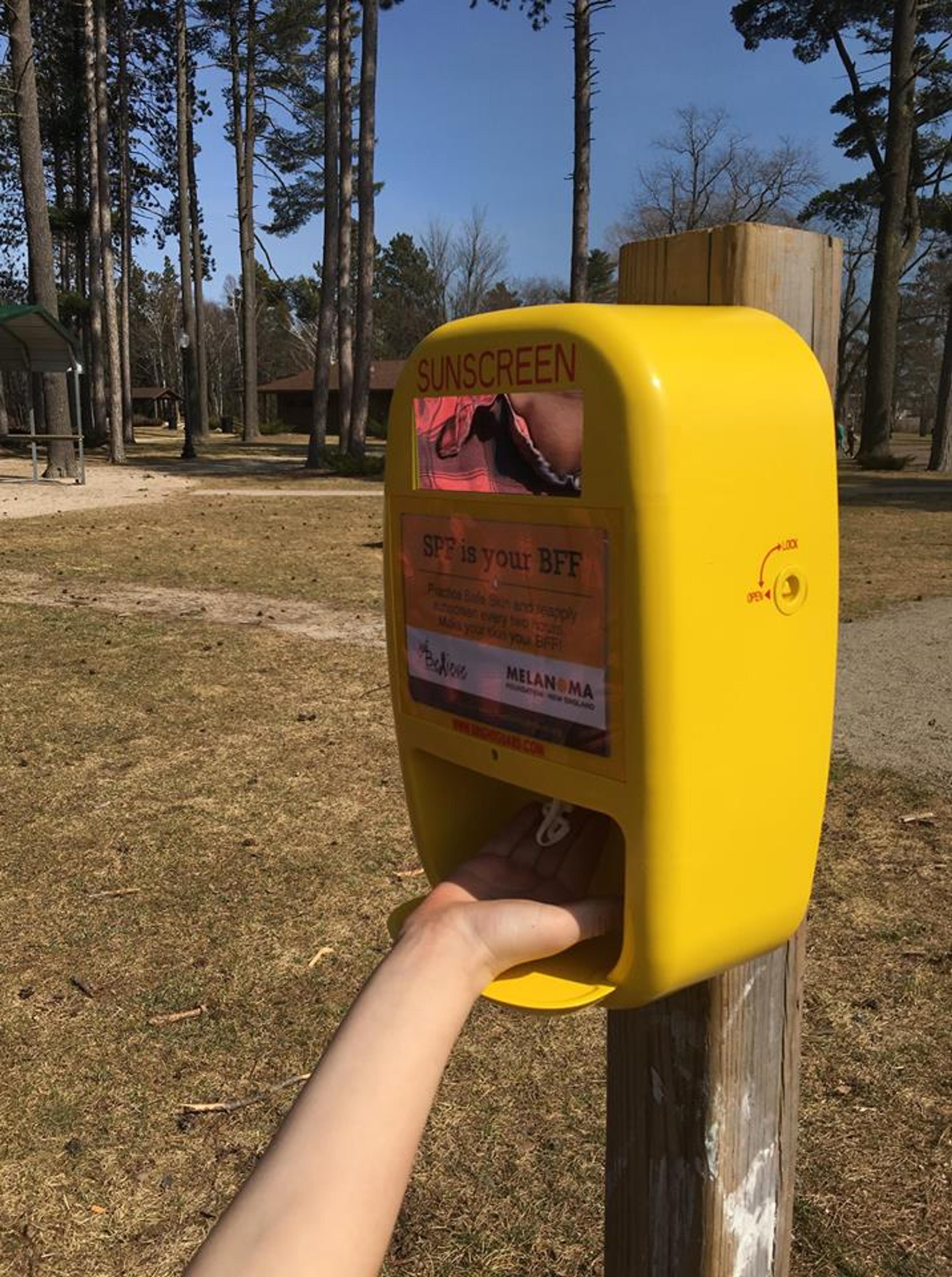 Image of a hand getting sunscreen from a bright yellow sunscreen dispenser. 