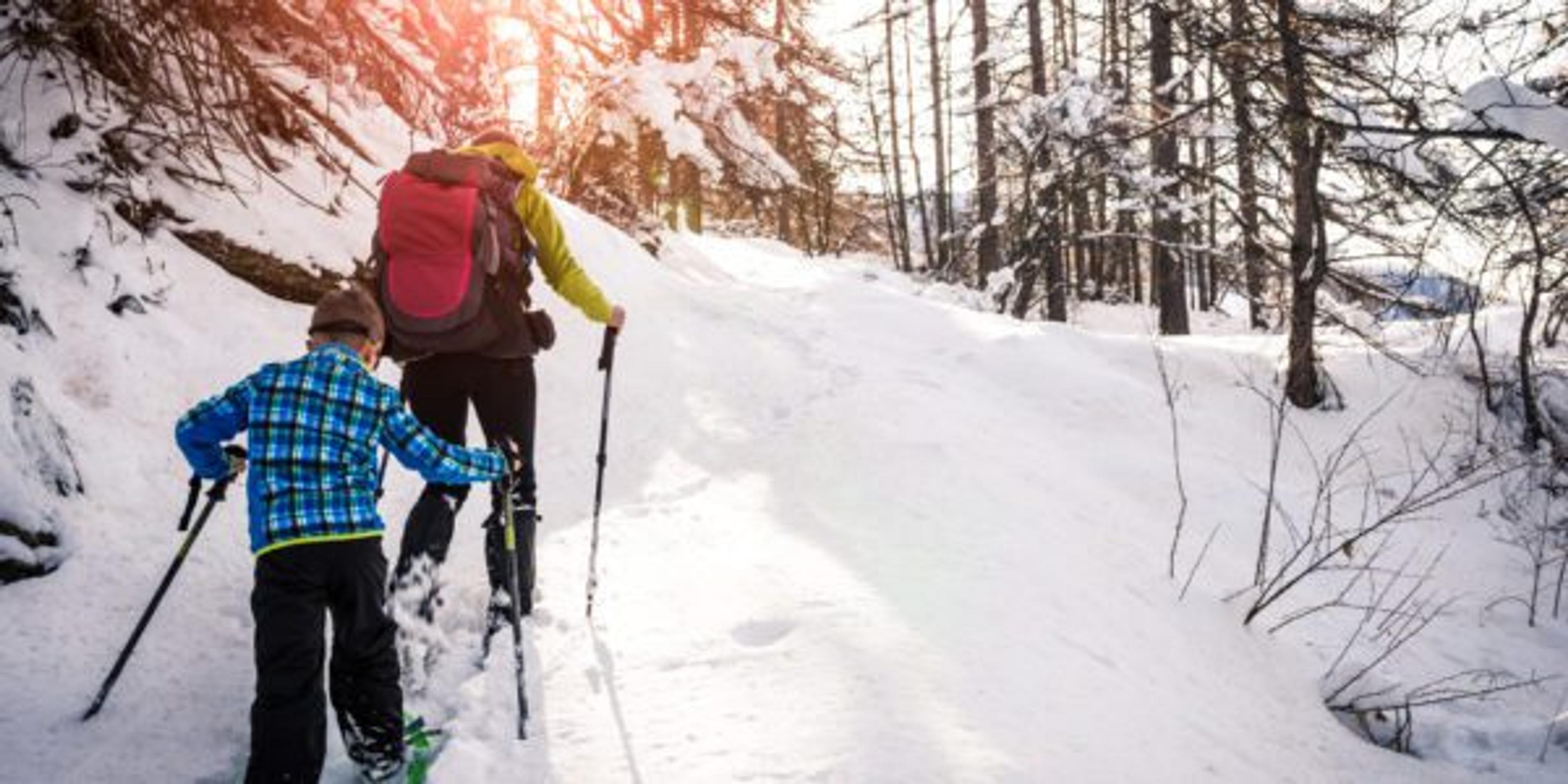 A woman and young boy snowshoe up a snow-covered hill.