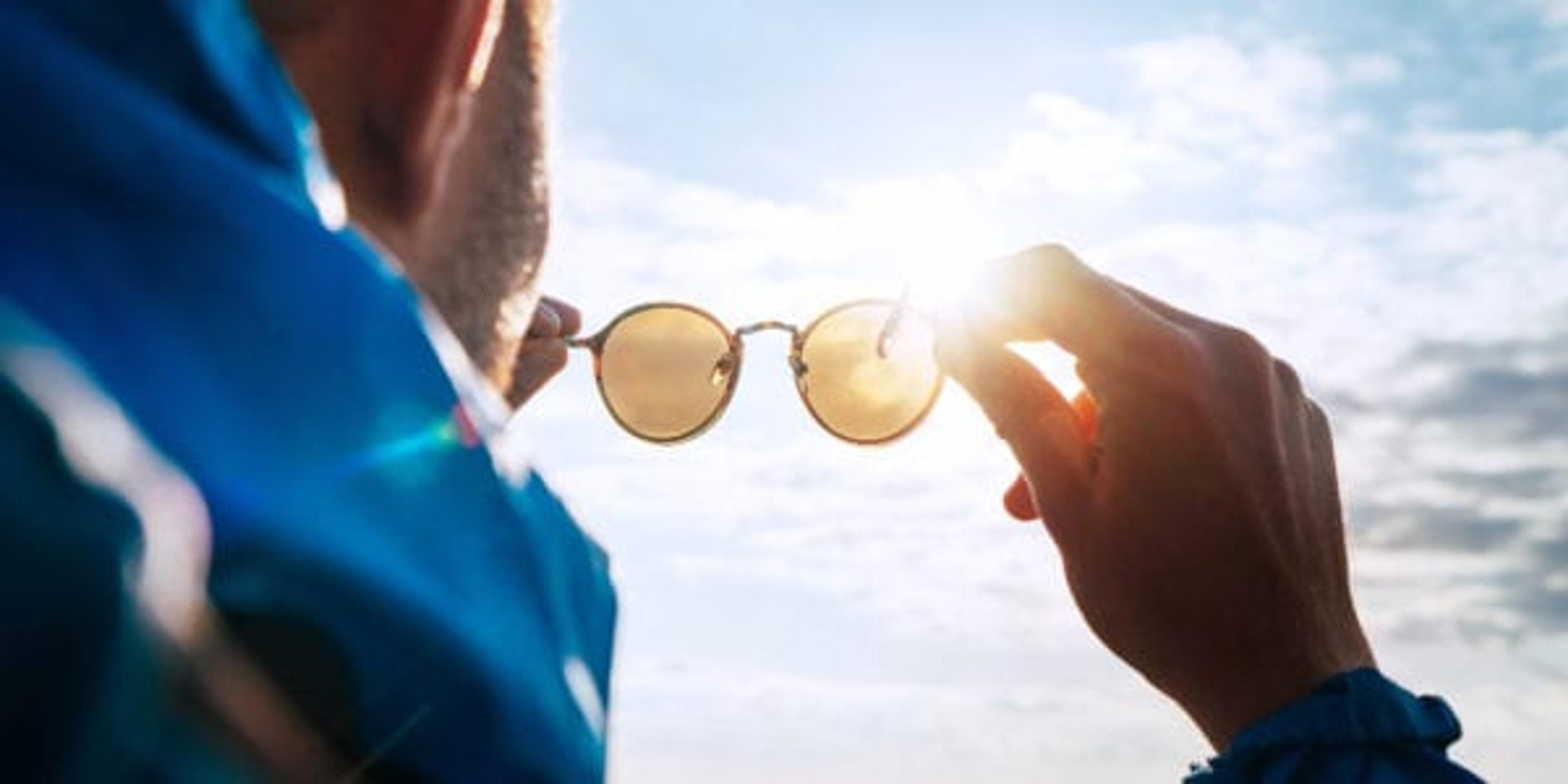 Backpacker man looking at bright sun through polarized sunglasses enjoying mountain landscape. Eye & Vision Care human health concept image.