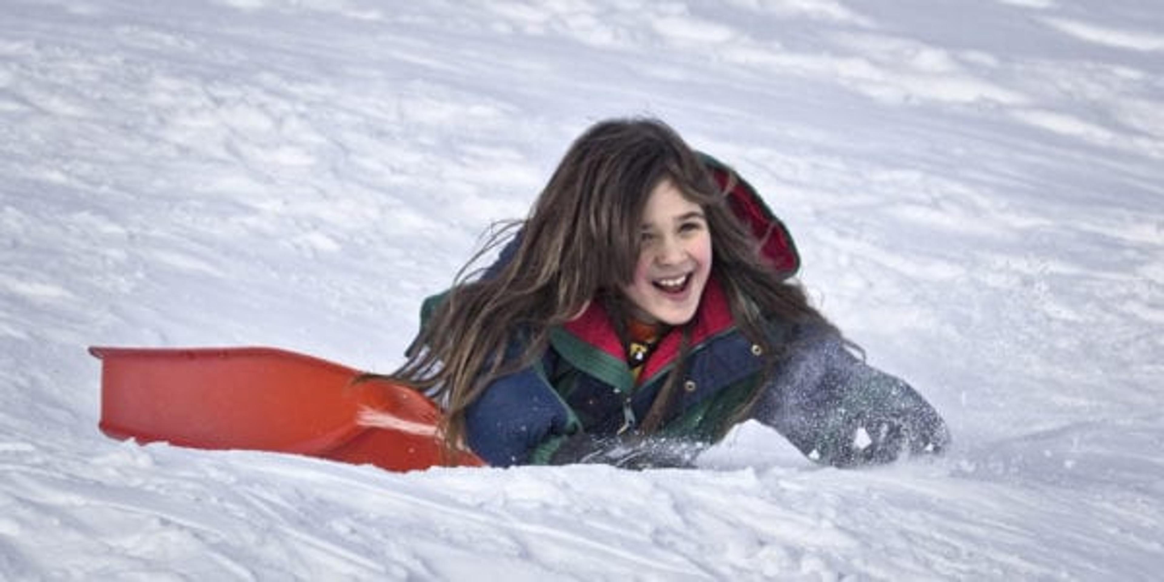 Little girl smiling while she sleds down a snow hill