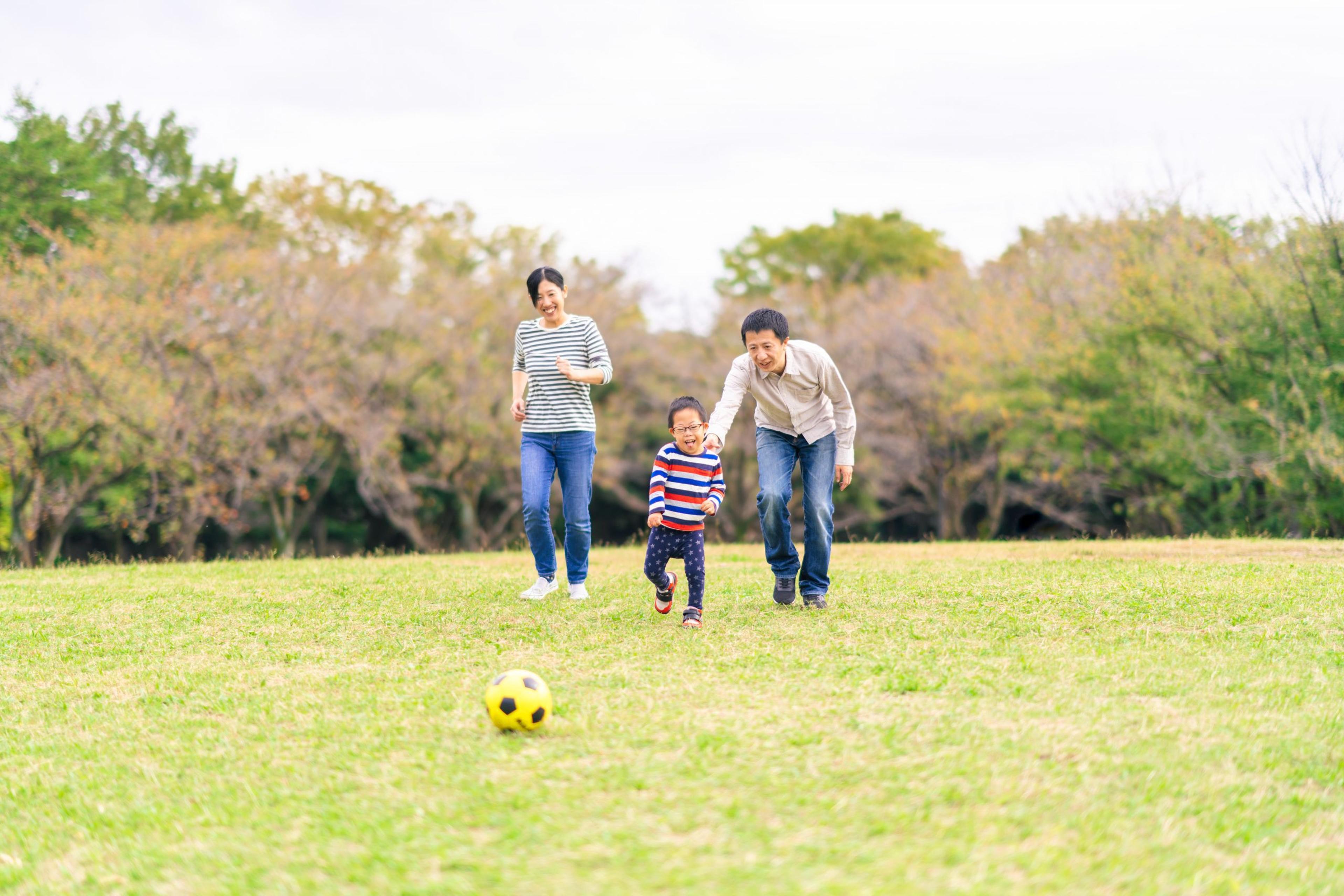 Family with a down syndrome boy is playing soccer in a public park.