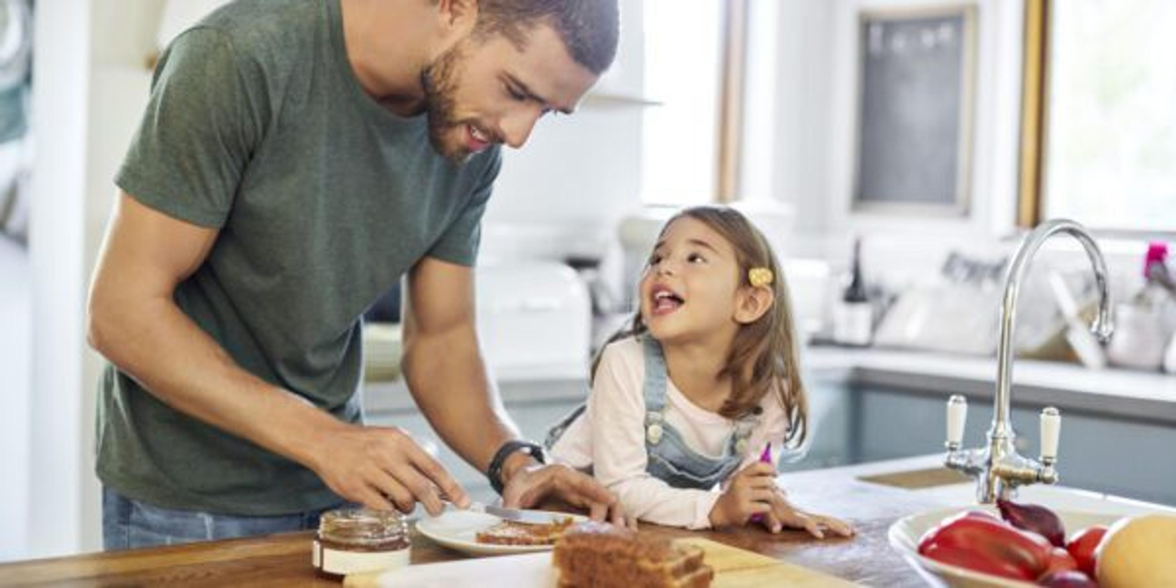 Man standing with daughter while making sandwich