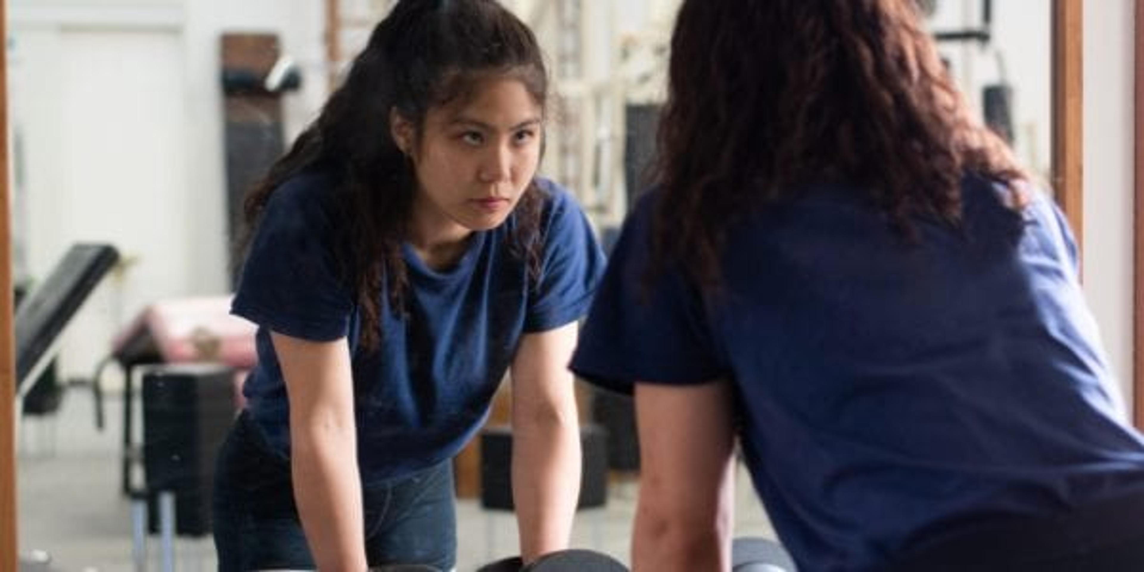 A medium shot of a female Japanese weightlifter looking at the mirror.