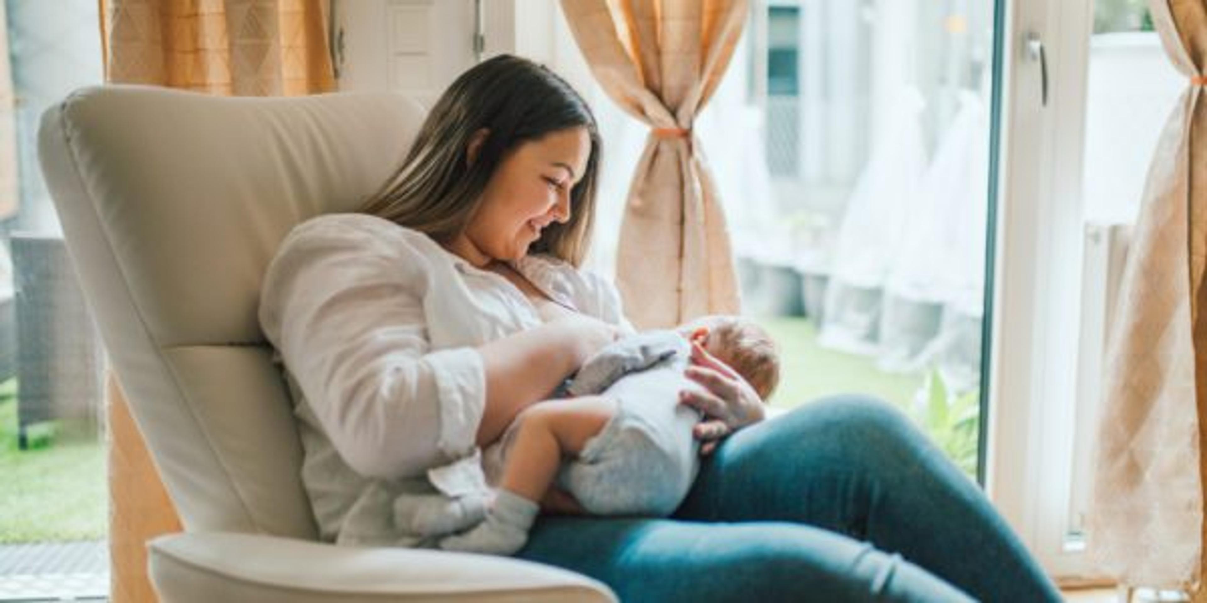 Mother breastfeeds and plays with her newborn baby