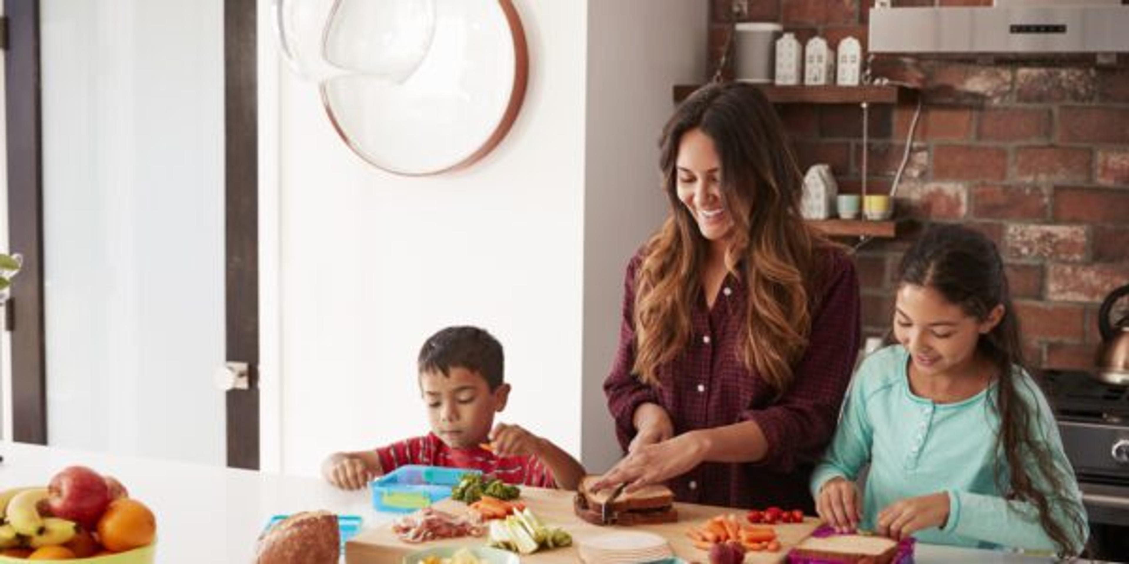 Children Helping Mother To Make School Lunches In Kitchen At Home