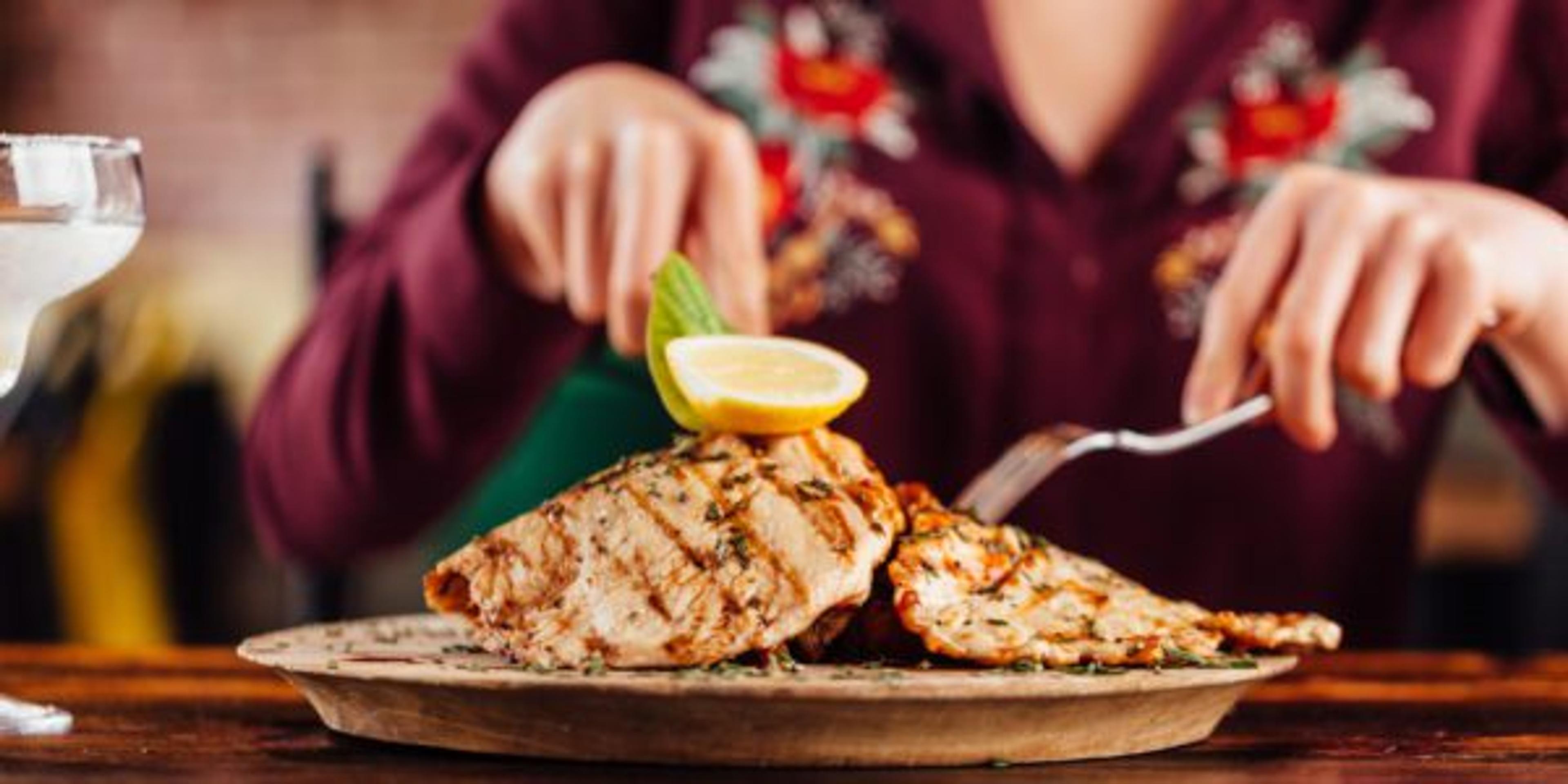 A woman slices into a plate of chicken breasts.