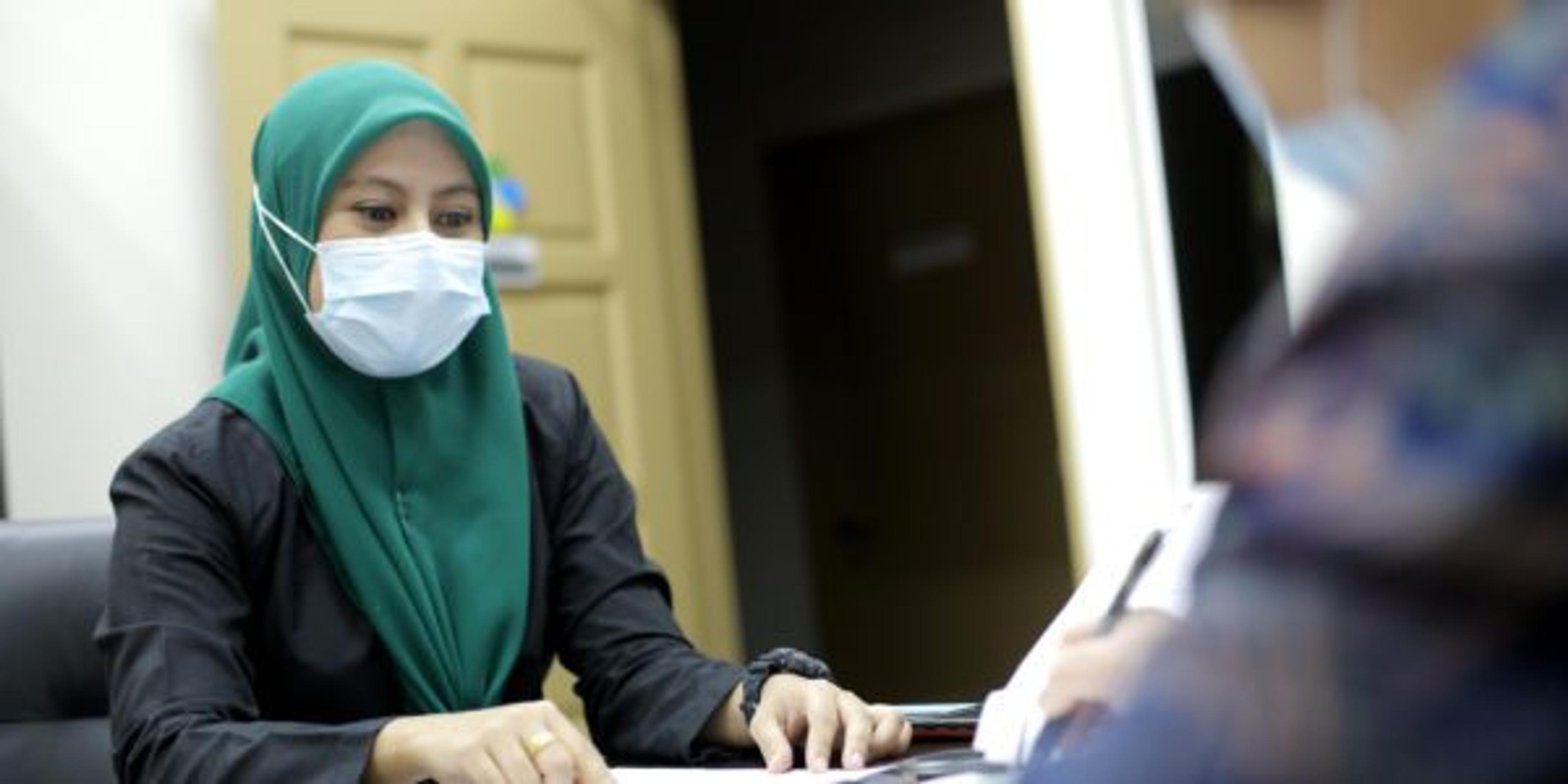 A Muslim female adult is selling insurance policy to Chinese lady in the office.
