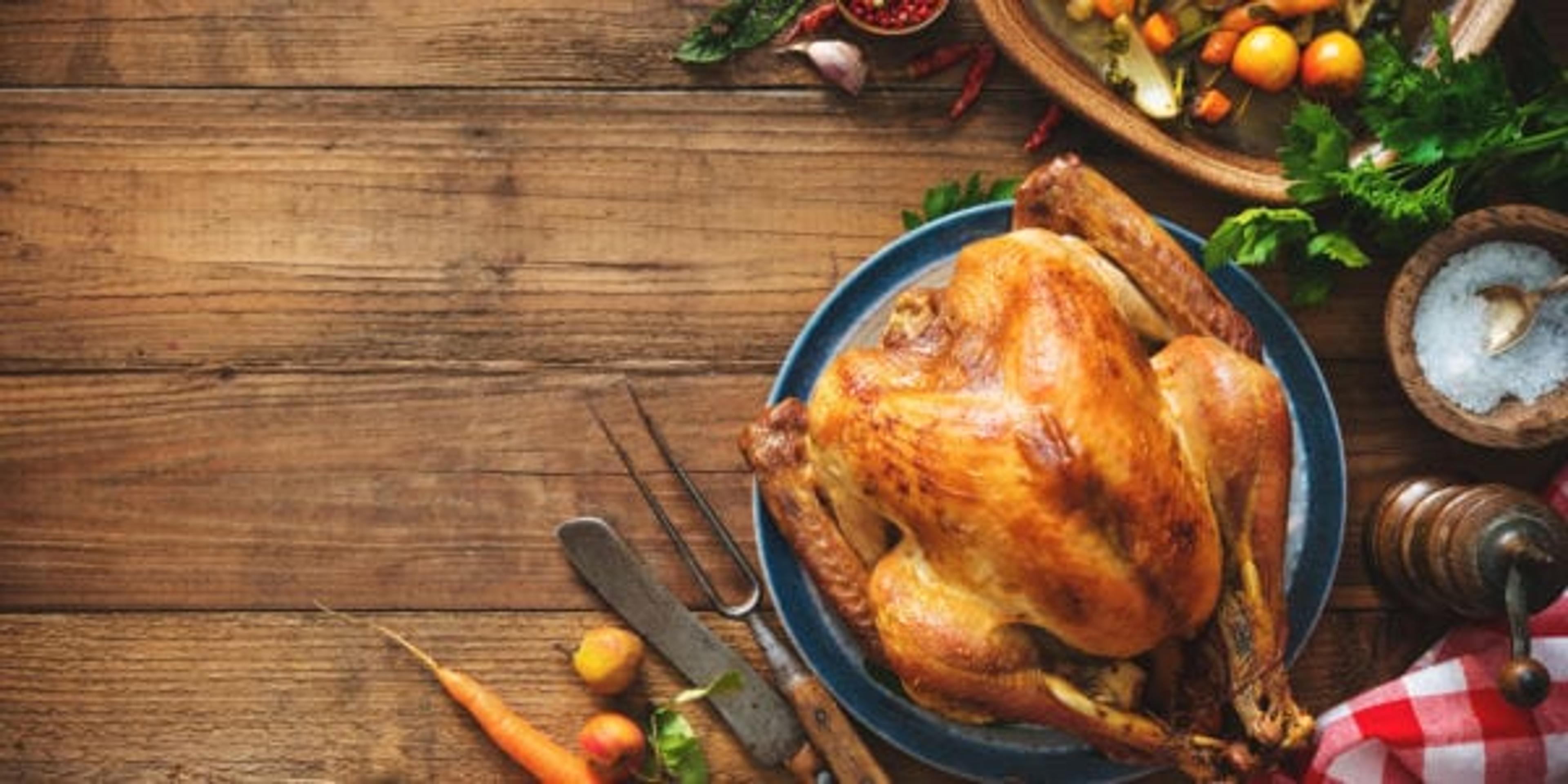 Thanksgiving turkey on a rustic wooden table surrounded by vegetables.