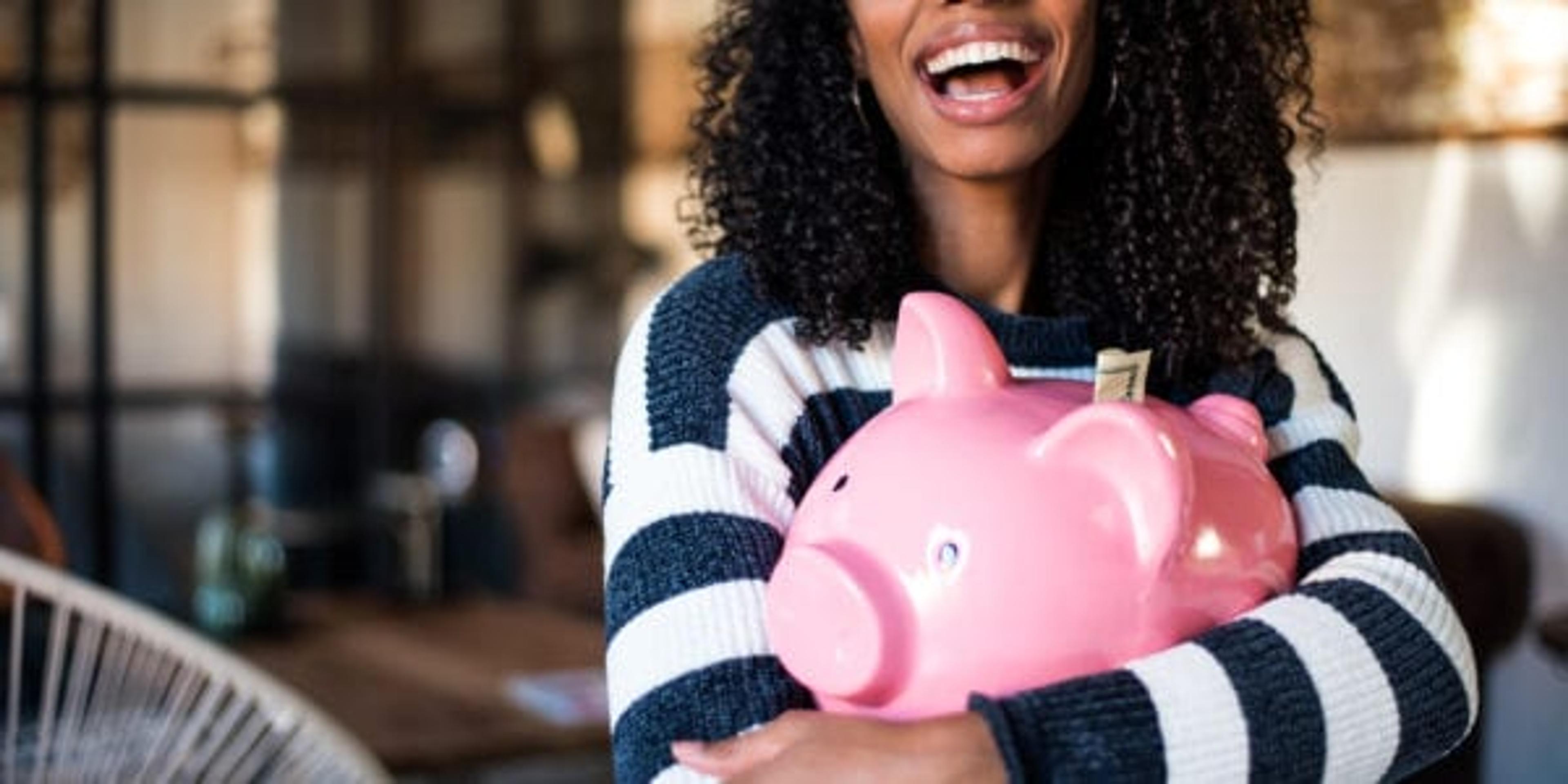 Black young woman hugging her pink piggy bank