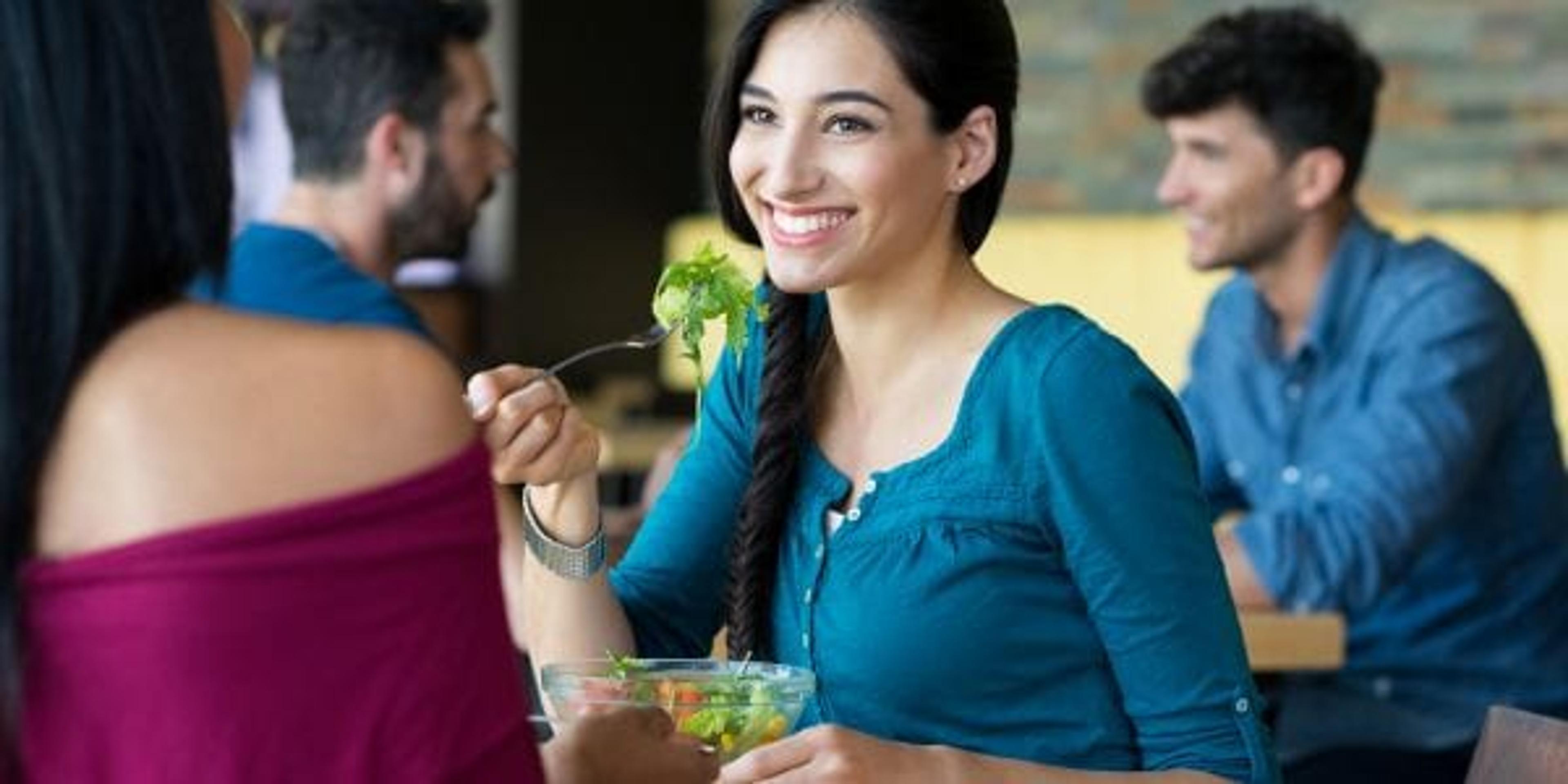 Young woman eating at a restaurant with a friend.