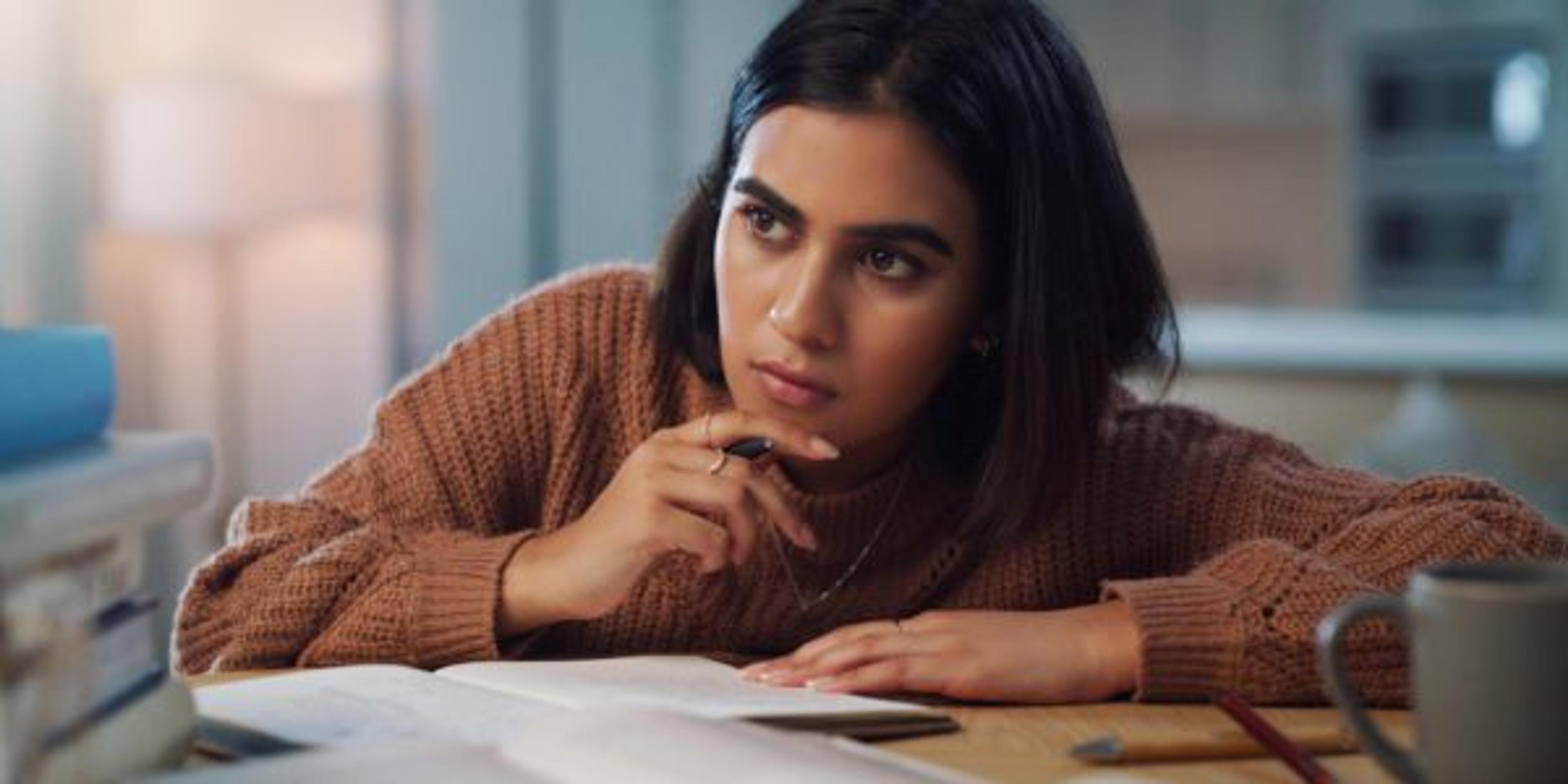 Shot of a young woman looking thoughtful while studying at home.