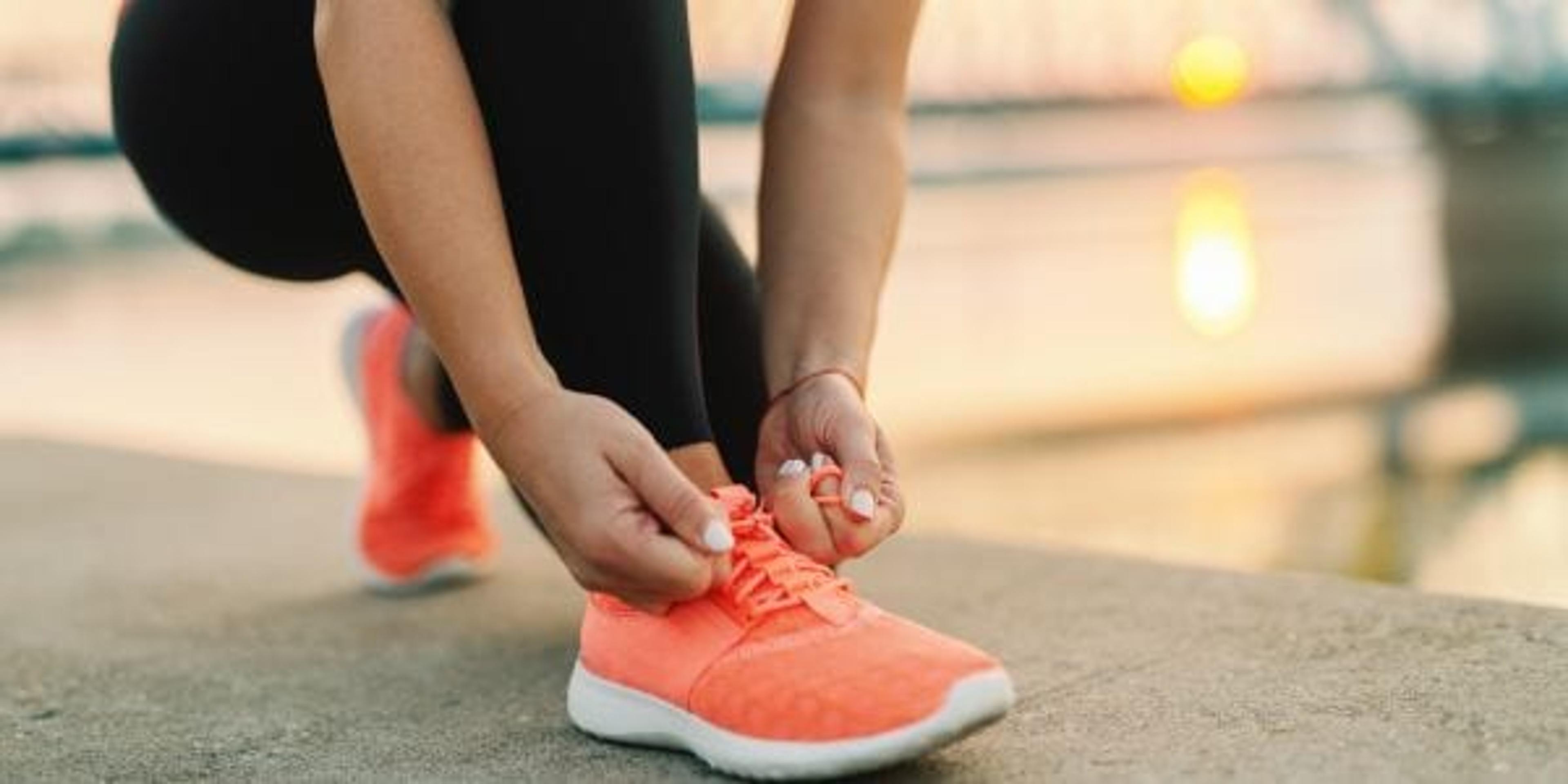 Close up of sporty woman tying shoelace while kneeling outdoor, In background bridge. Fitness outdoors concept.