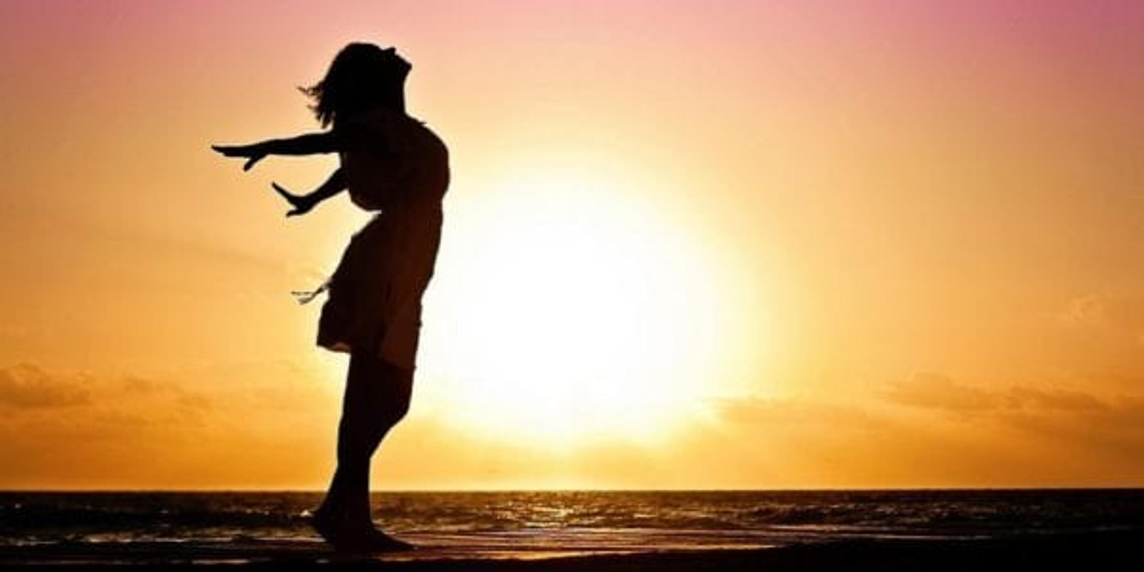 woman standing facing the sky with a sunset in the background