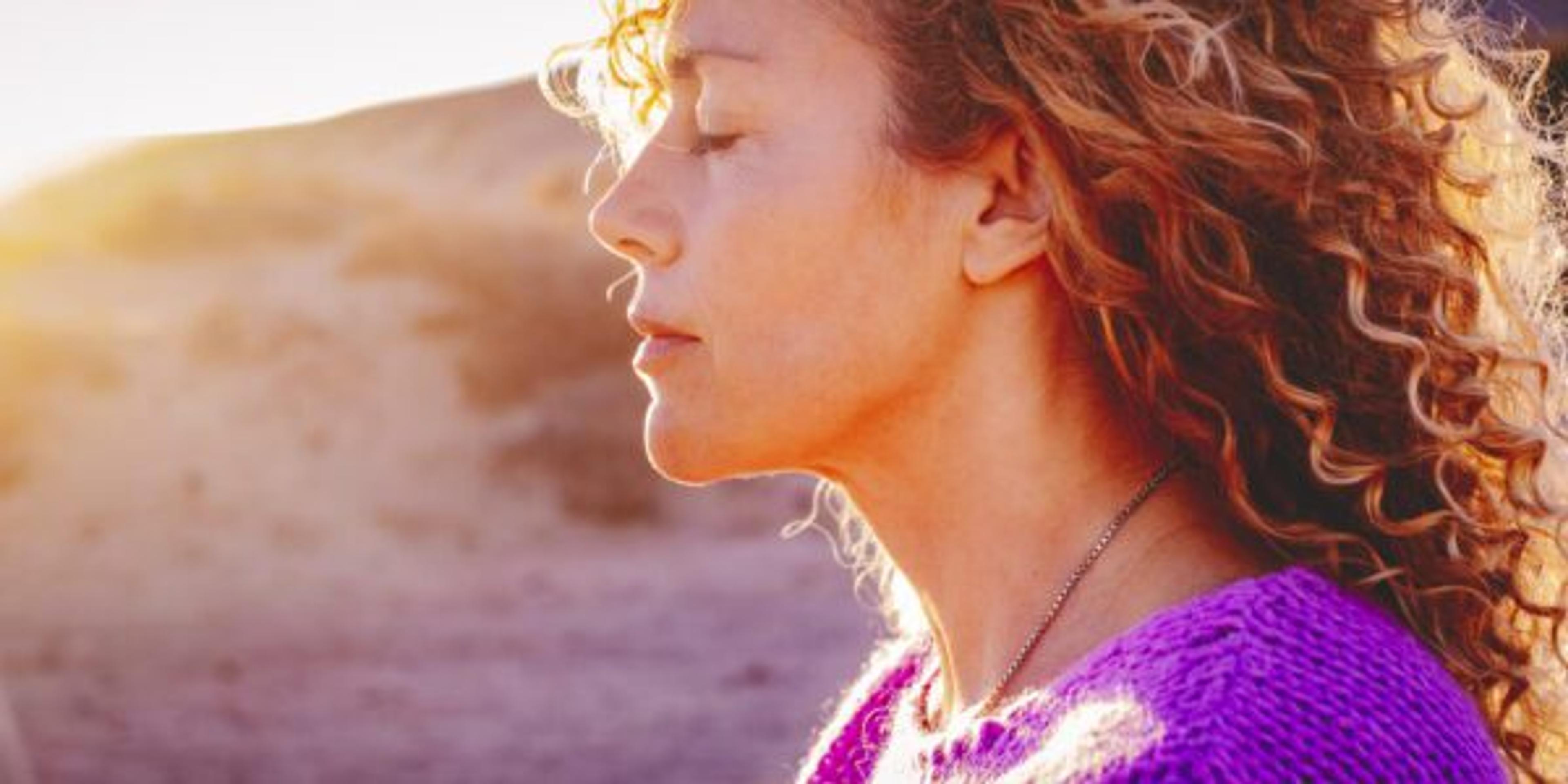 Close up sunset portrait of attractive woman with closed eyes and sun in back light. Dreaming and enjoying feeling concept lifestyle emotion. Serene female people outdoor with curly hair