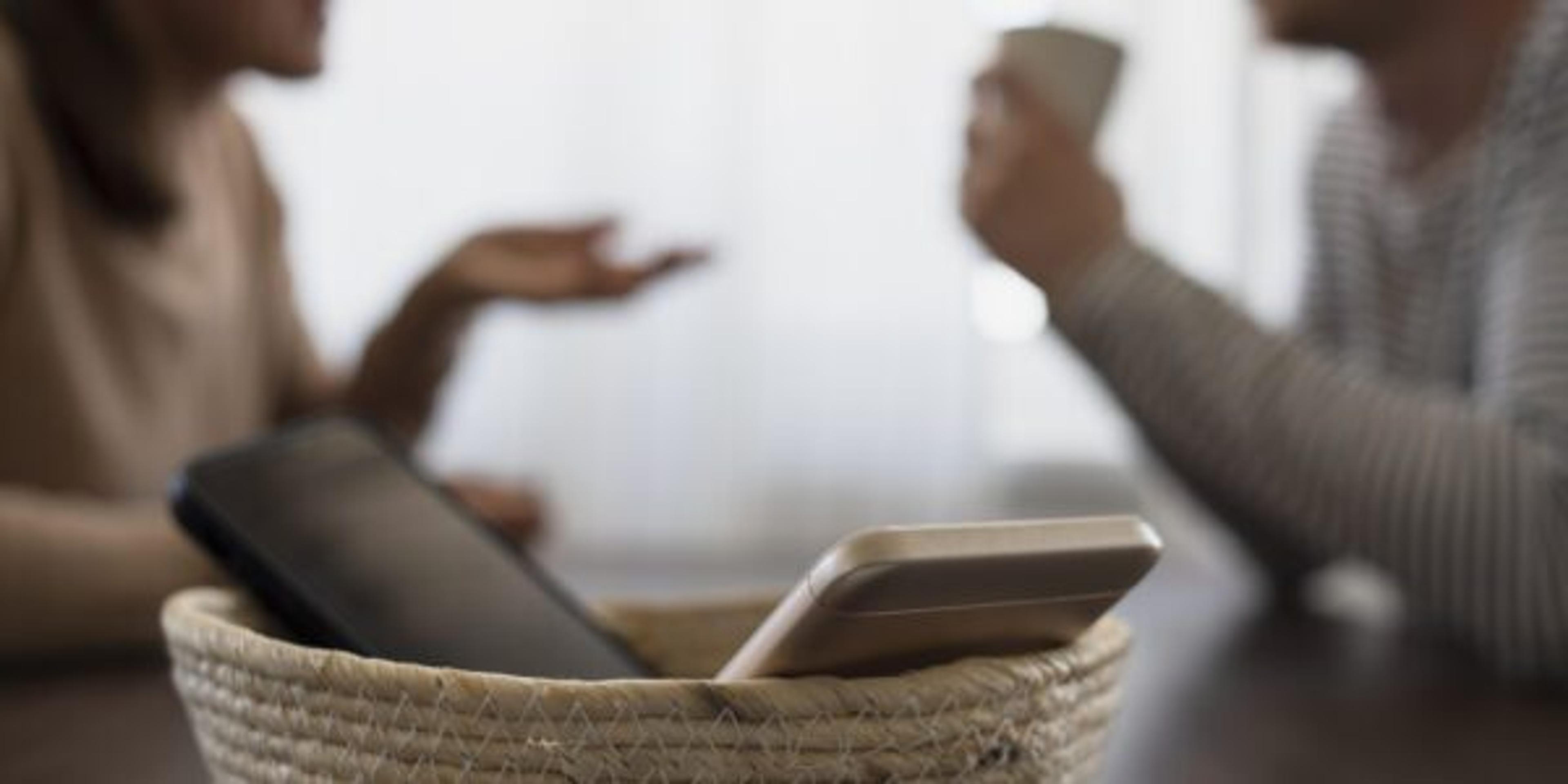 Two people chat over coffee with their phones tucked away in a nearby basket.