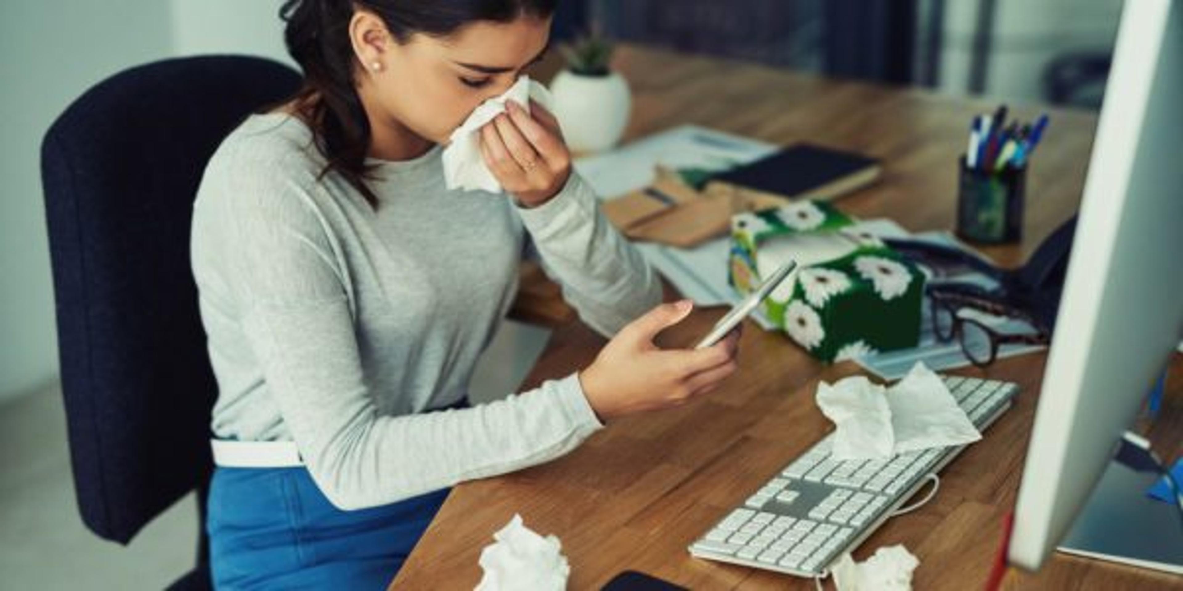 Shot of a young businesswoman blowing her nose while texting on a cellphone in an office