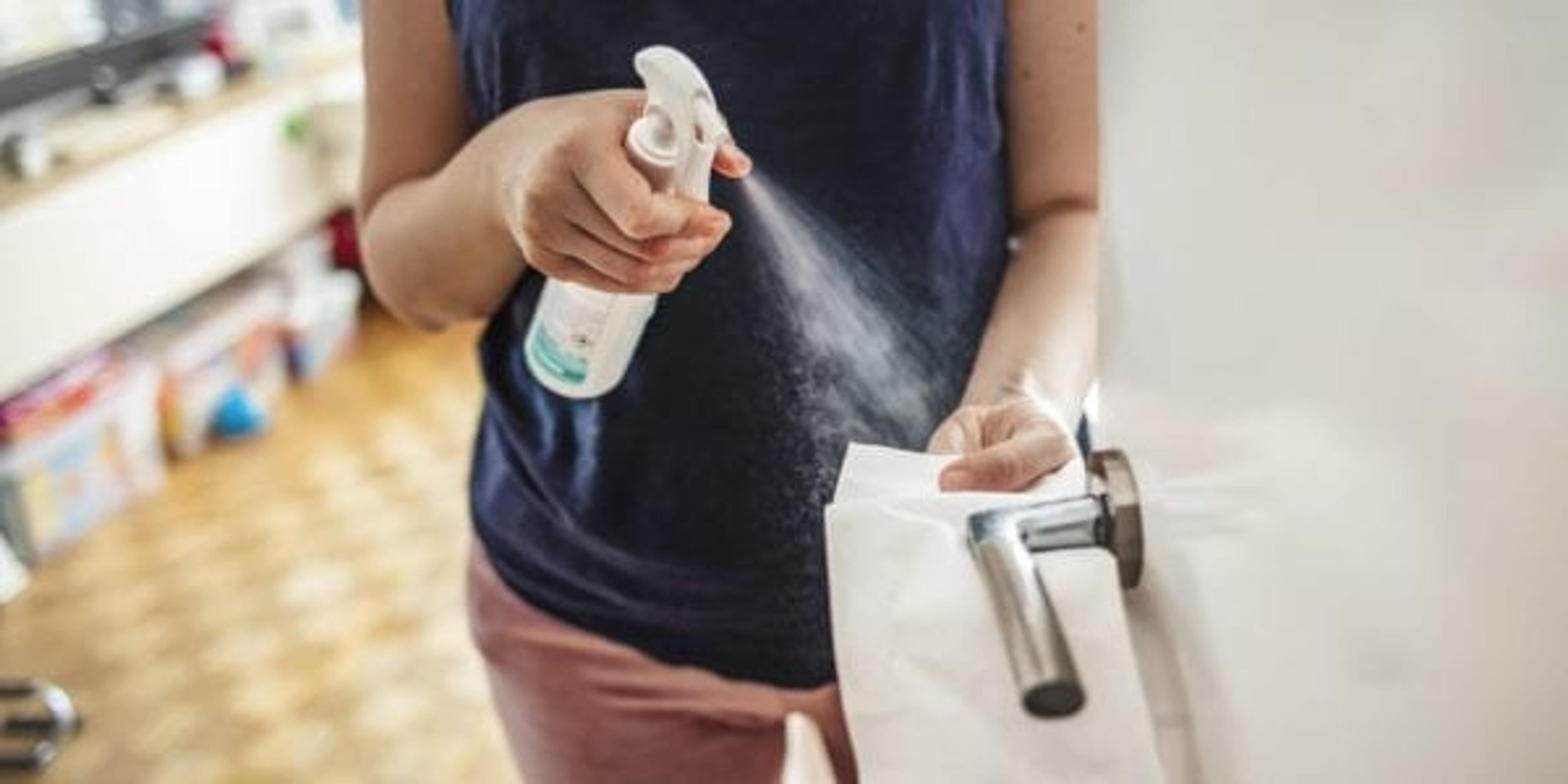 Woman spraying cleaner on door knob