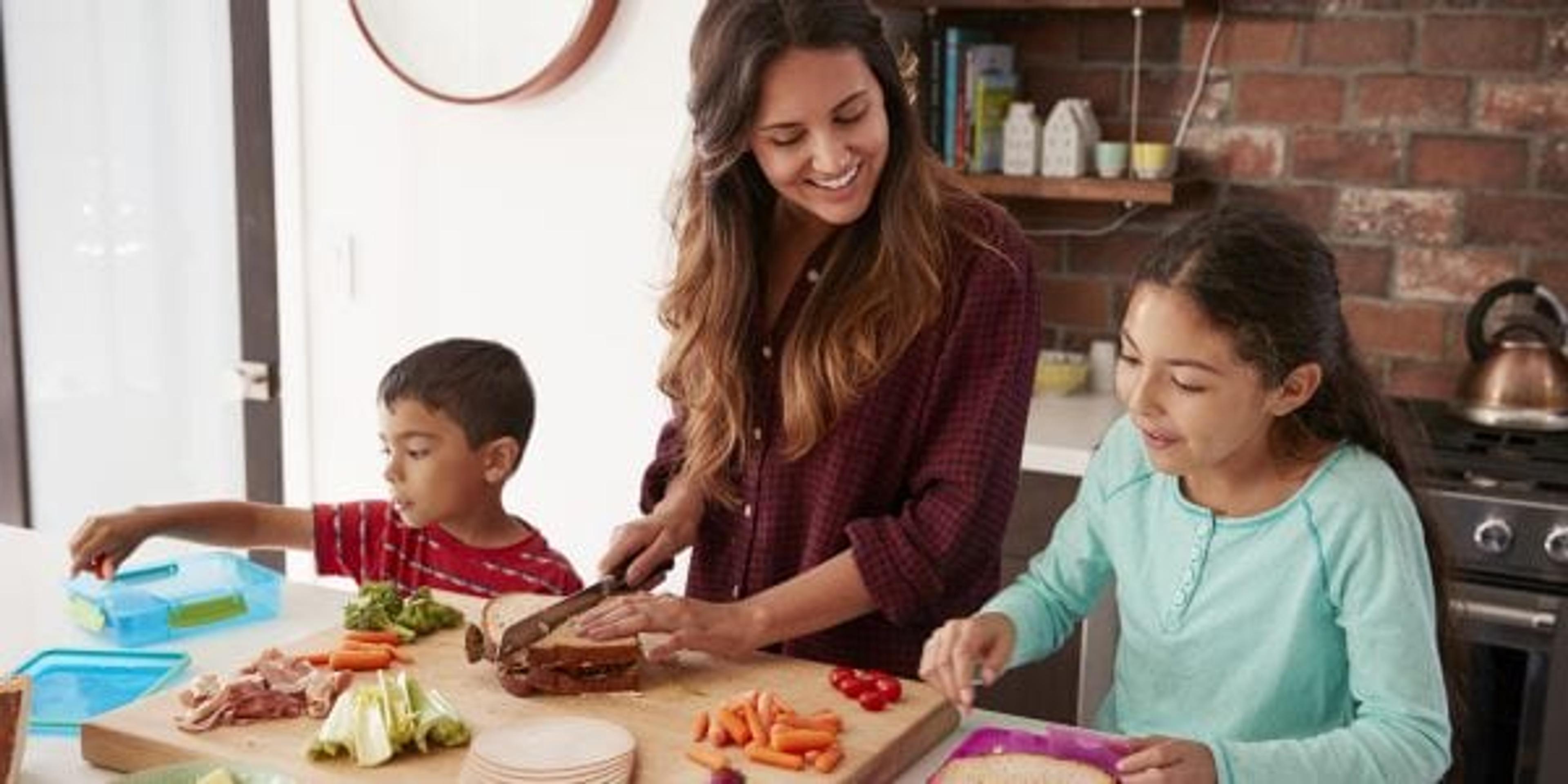 Children Helping Mother To Make School Lunches In Kitchen At Home