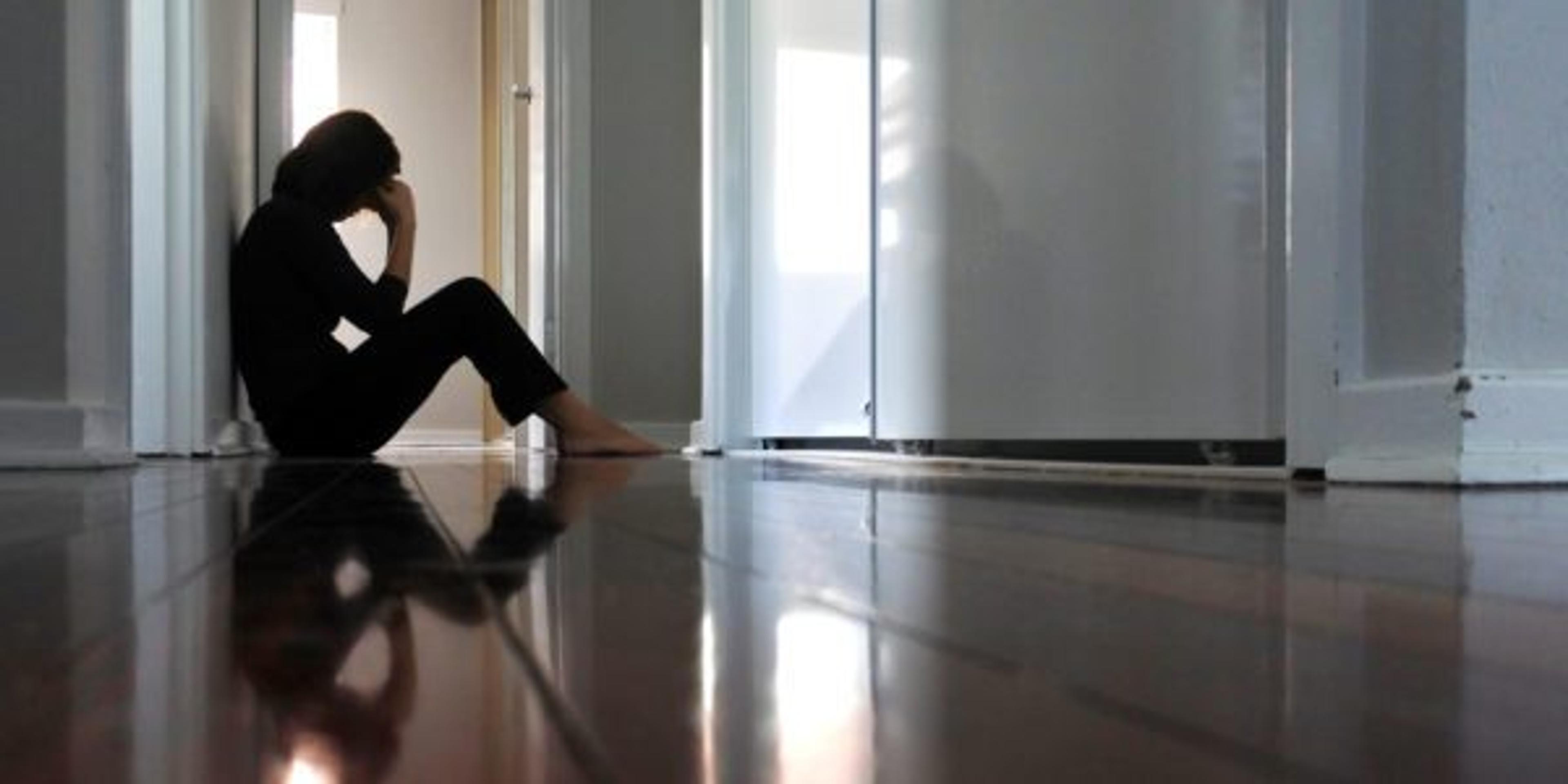 Sad woman sitting on dark home corridor floor.