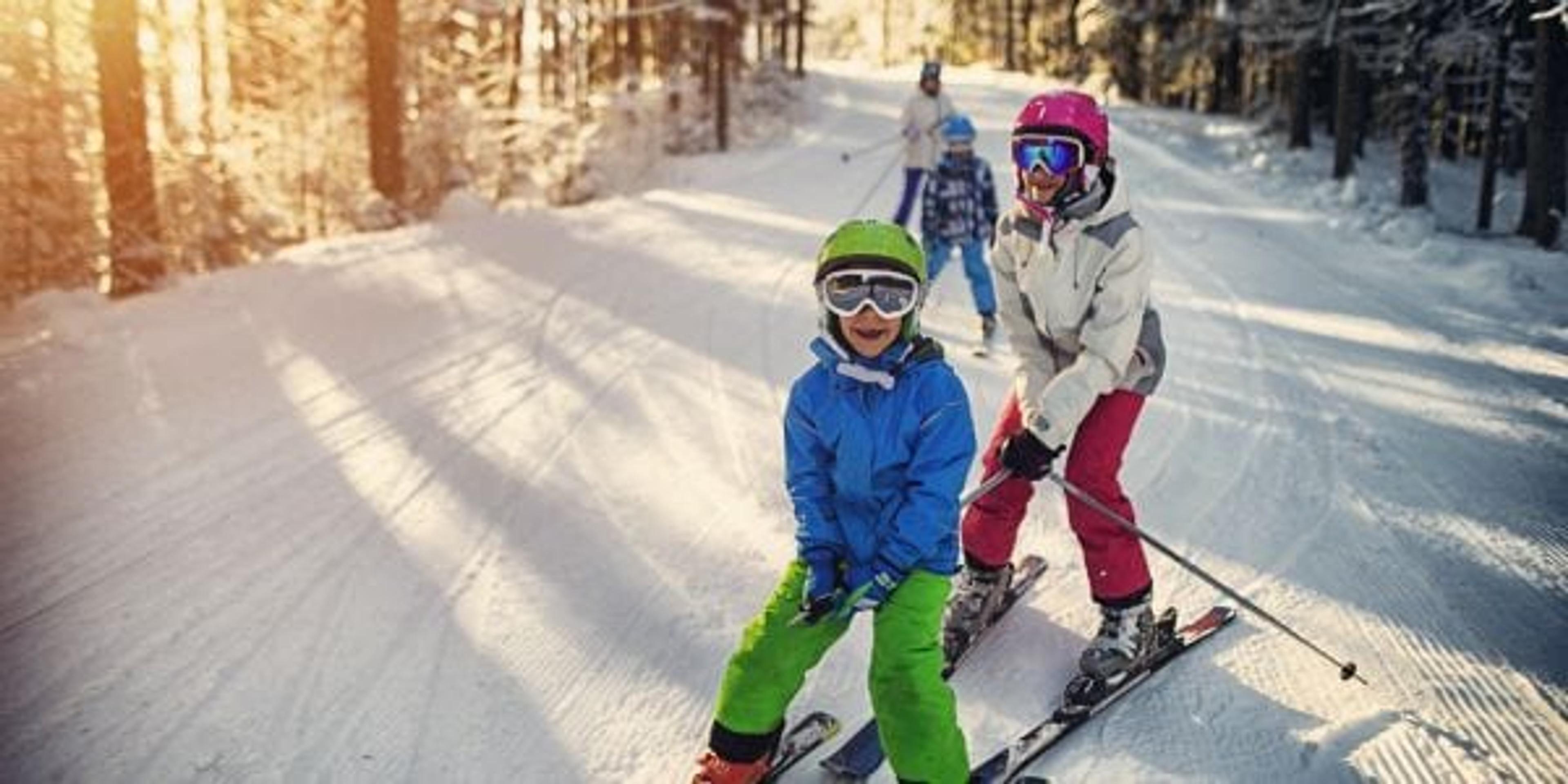 Mother with kids are skiing together down the ski slope. Everybody is laughing happily.